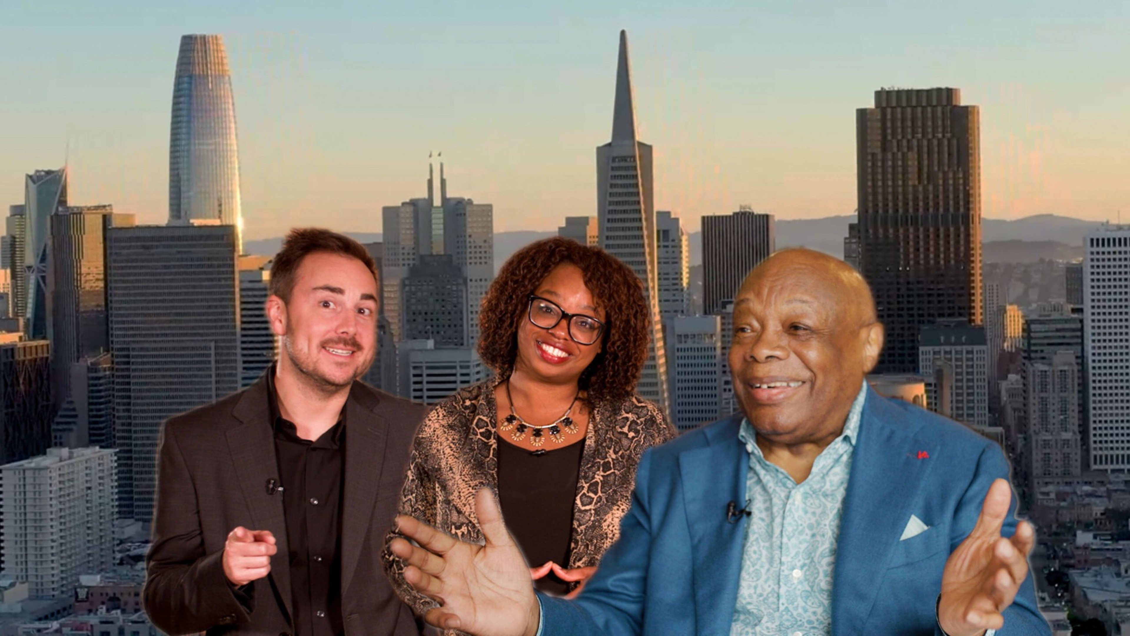 Three people smile and pose in front of a city skyline at sunset, with one man in a blue suit gesturing broadly and a woman in glasses in the center.