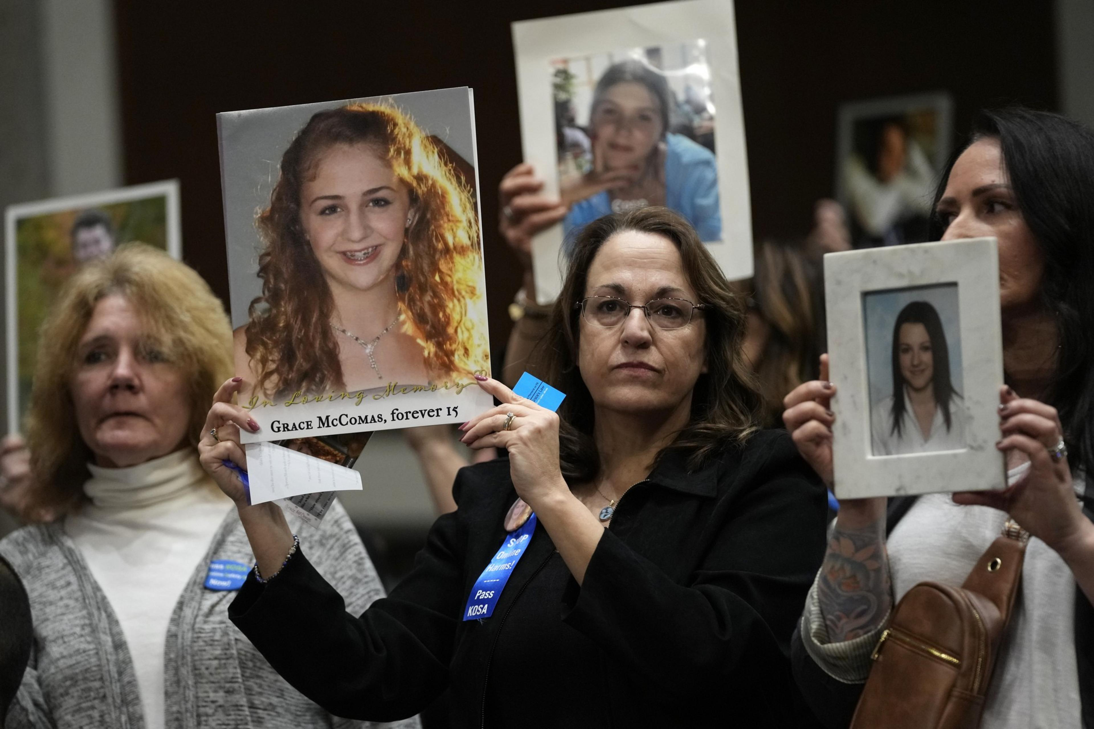Women wearing blue ribbons hold up pictures of young people