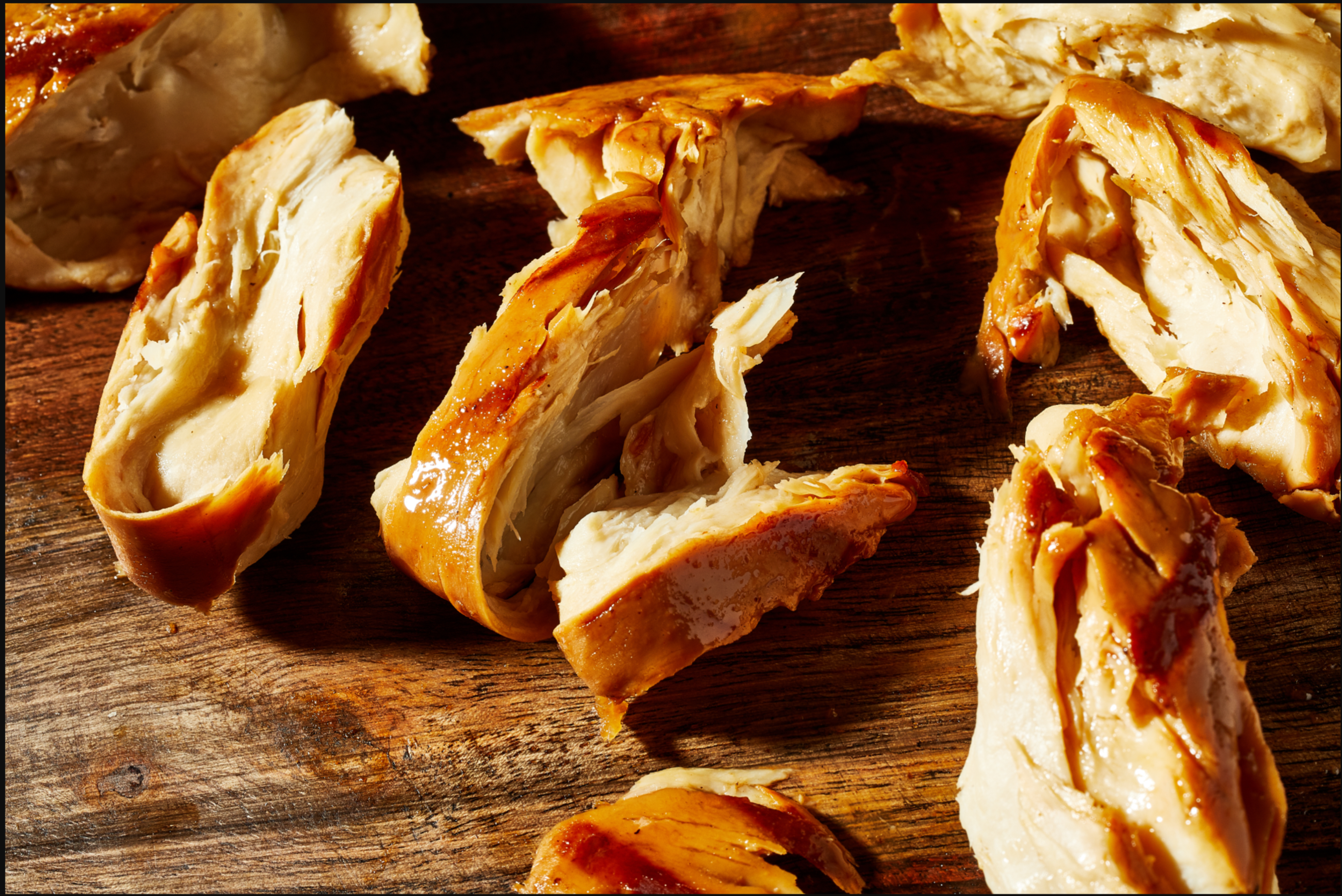 Several pieces of golden-brown cooked chicken are scattered on a wooden surface, showing tender and juicy meat with crispy edges.