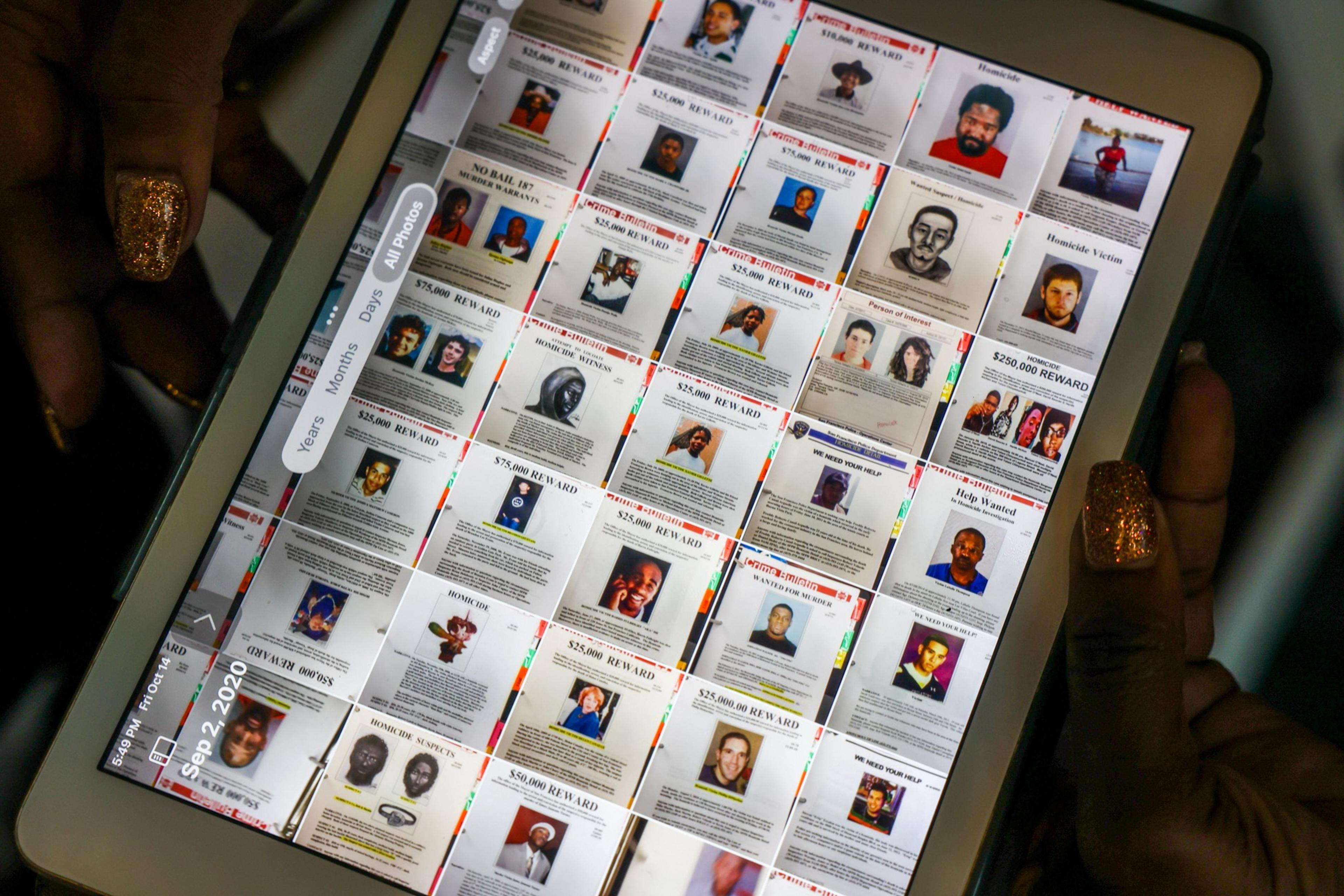 The image shows a computer screen displaying various wanted posters with photos and reward amounts. A hand with glittery nails is holding the screen.