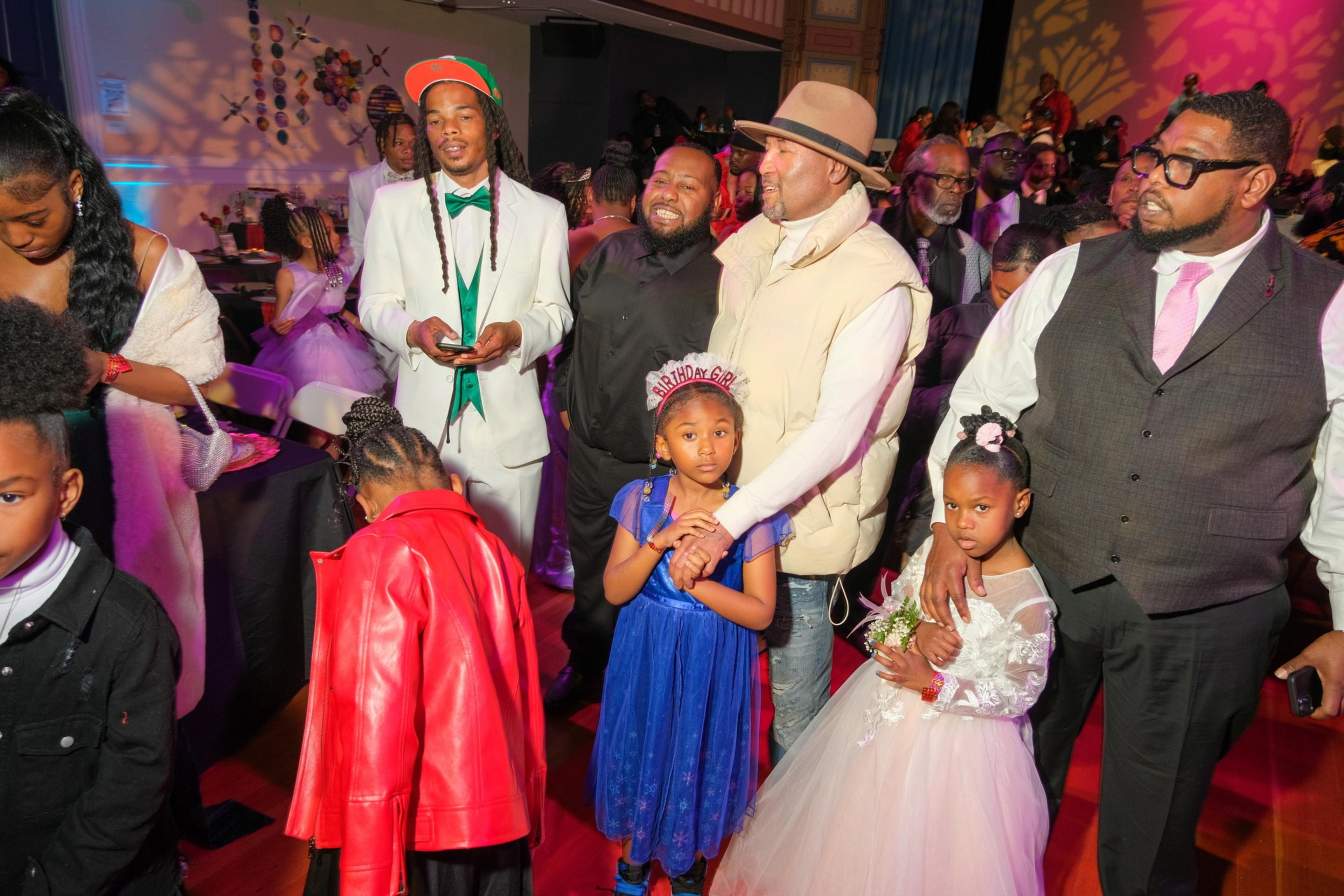 A lively group of adults and children dressed up for a celebration with colorful lights and decorations.