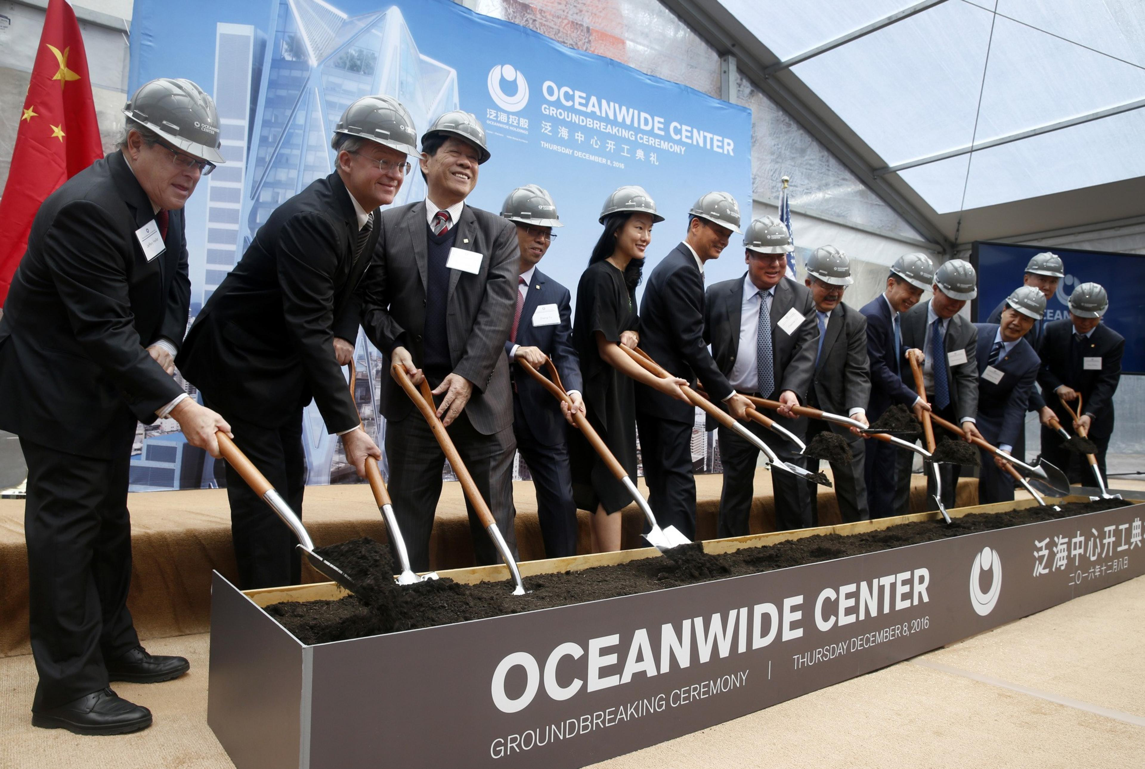 Group of people in suits and hard hats at a ceremonial groundbreaking.