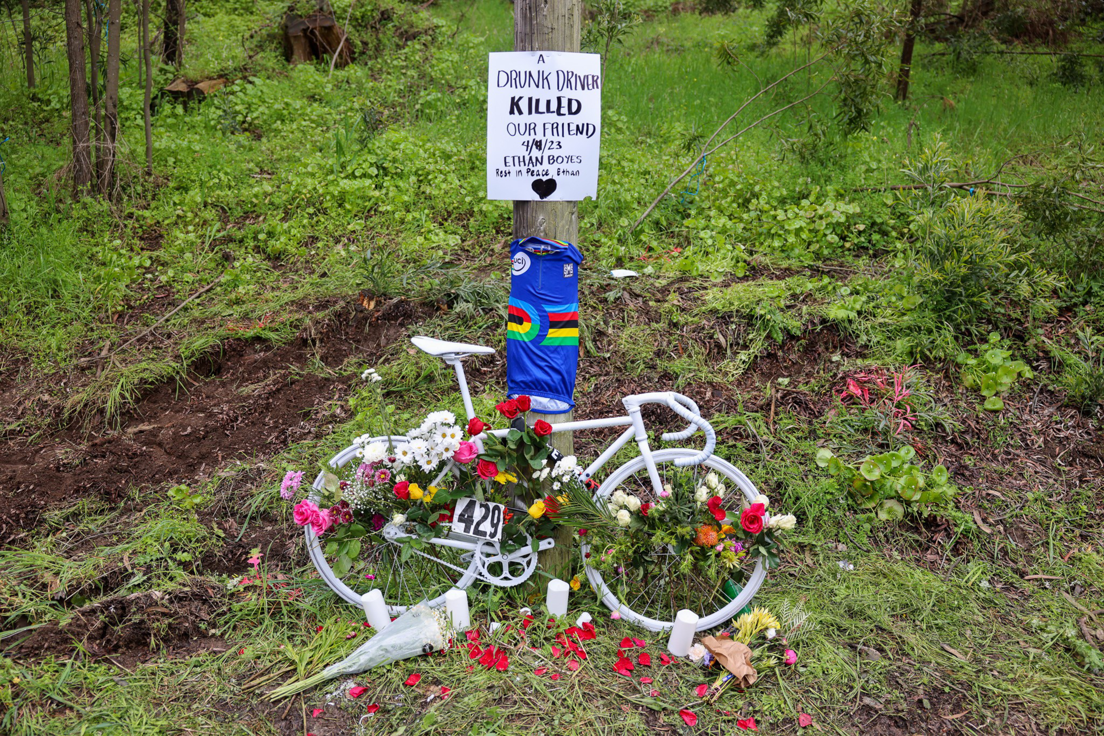 A bicycle painted white and adorned with flowers leans against a tree.