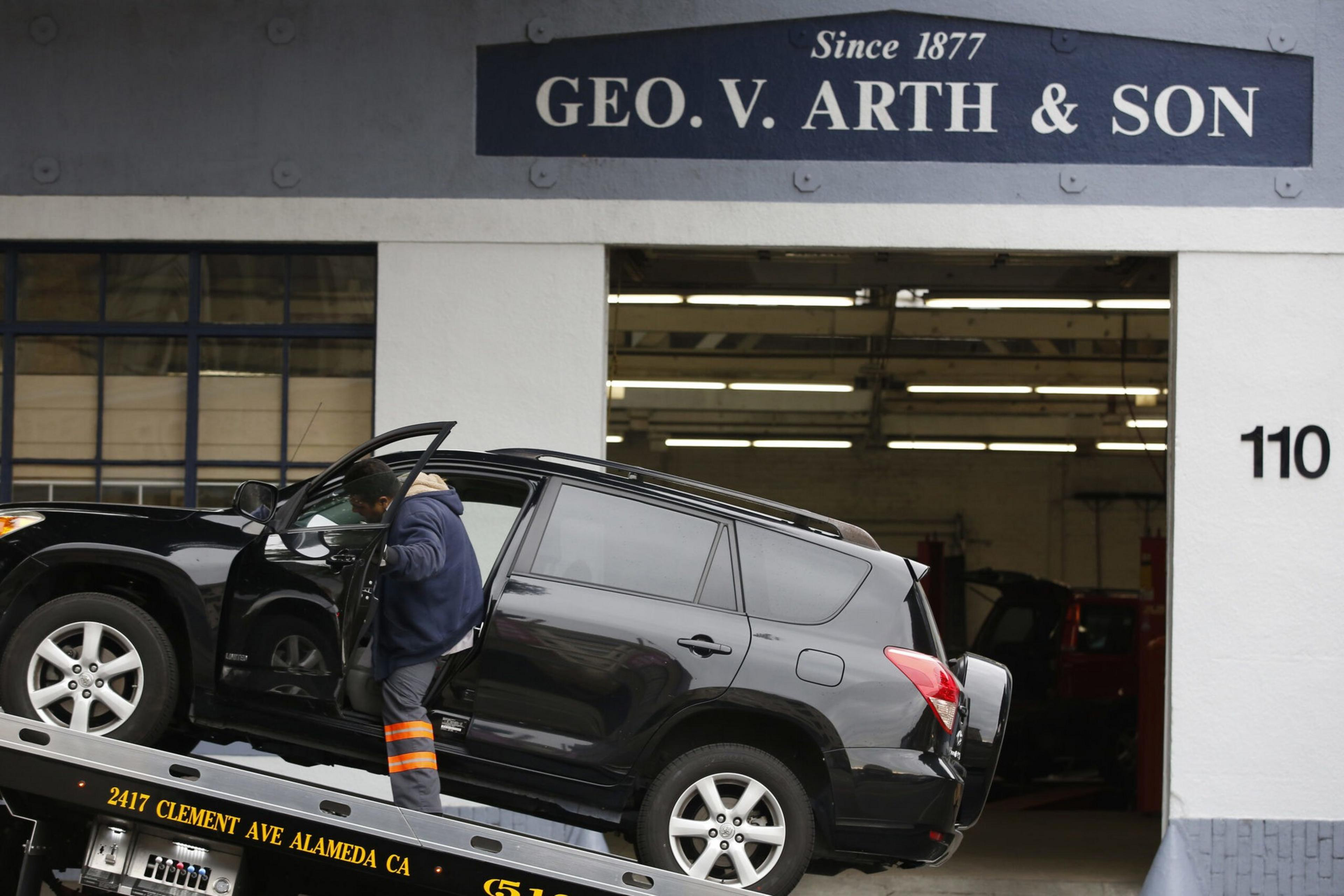 A black SUV is being loaded onto a tow truck by a person wearing a jacket and reflective pants, outside a building marked "GEO. V. ARTH & SON."