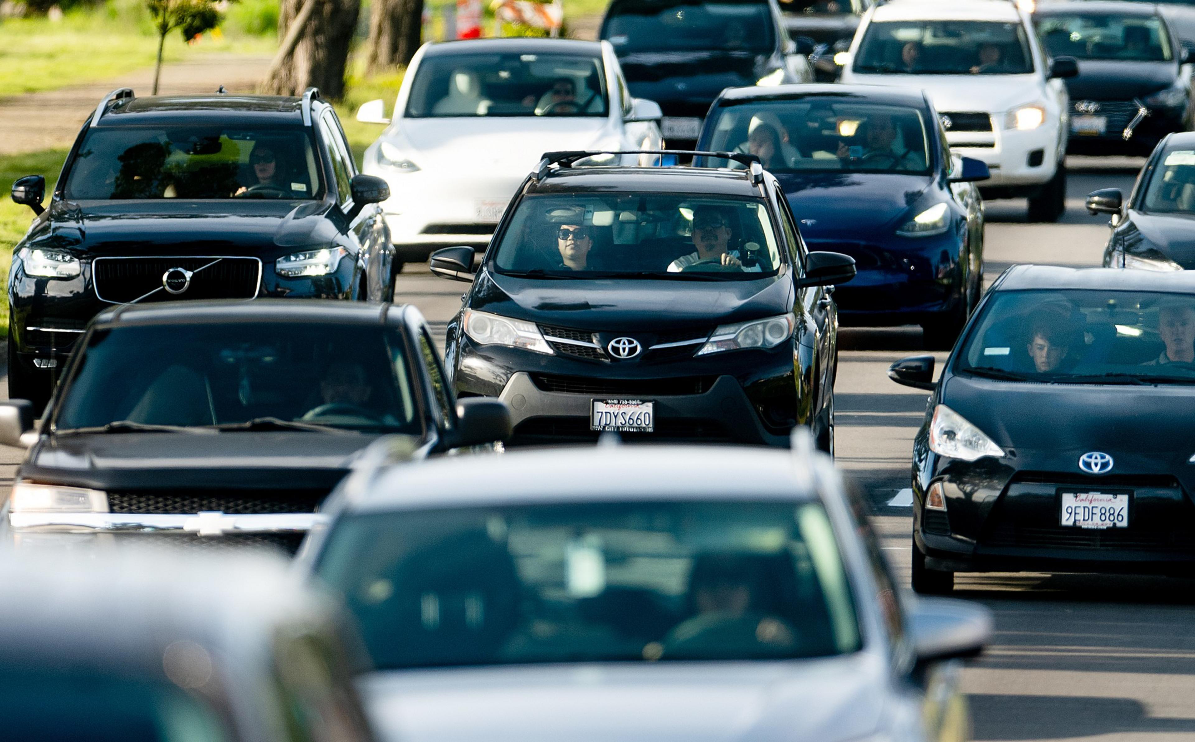 A busy road with cars in traffic, showing various vehicles including a black Toyota and other cars in close proximity, with people visible inside.
