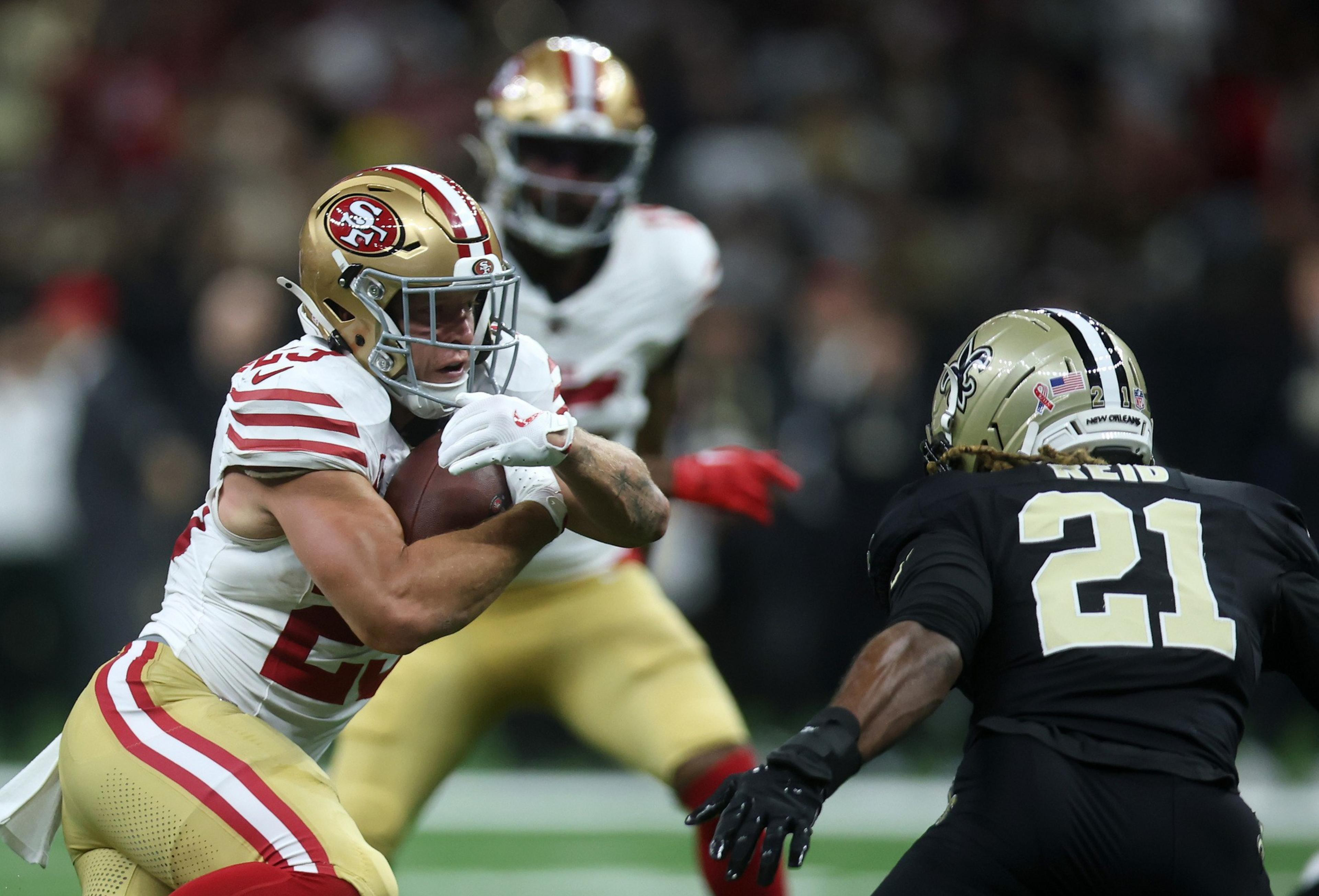 A San Francisco 49ers player tightly holds the football as he prepares to evade a New Orleans Saints defender wearing number 21.