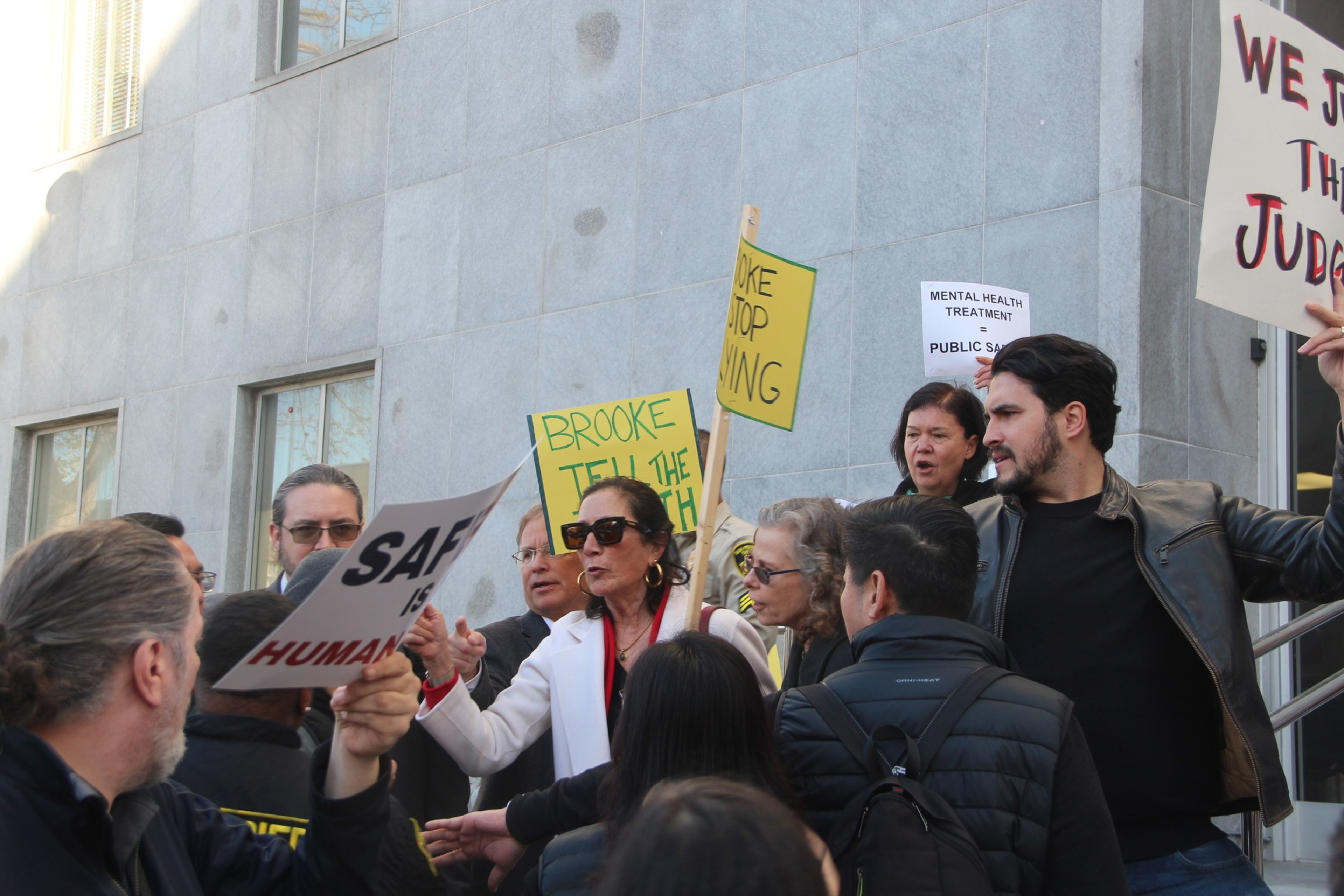 A group of people protesting with signs, some reading "SAFE HUMAN", "BROOKE TELL THE TRUTH", and "MENTAL HEALTH TREATMENT NOT JAIL".