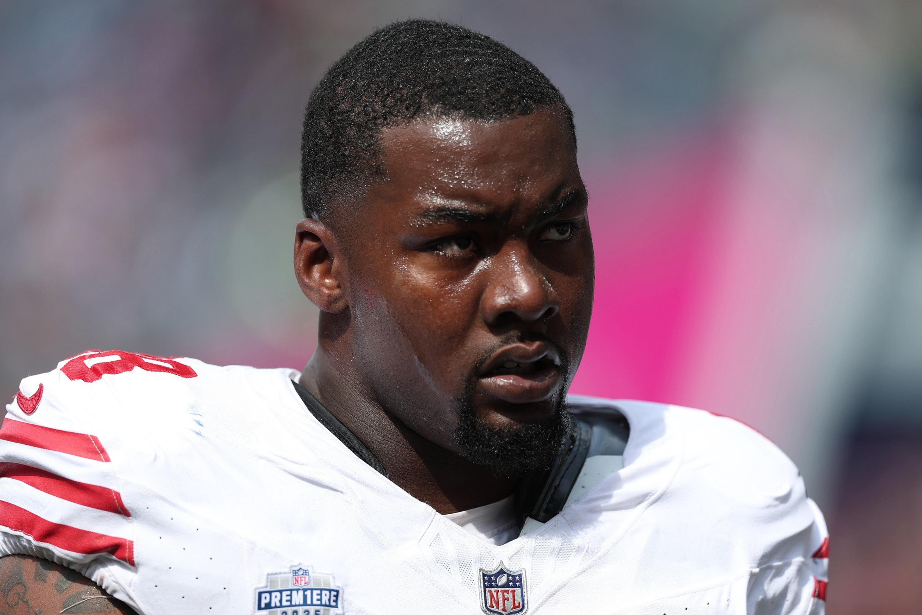 A focused football player in a white jersey with red stripes, sweating under bright light, looks intensely to the side during a game.