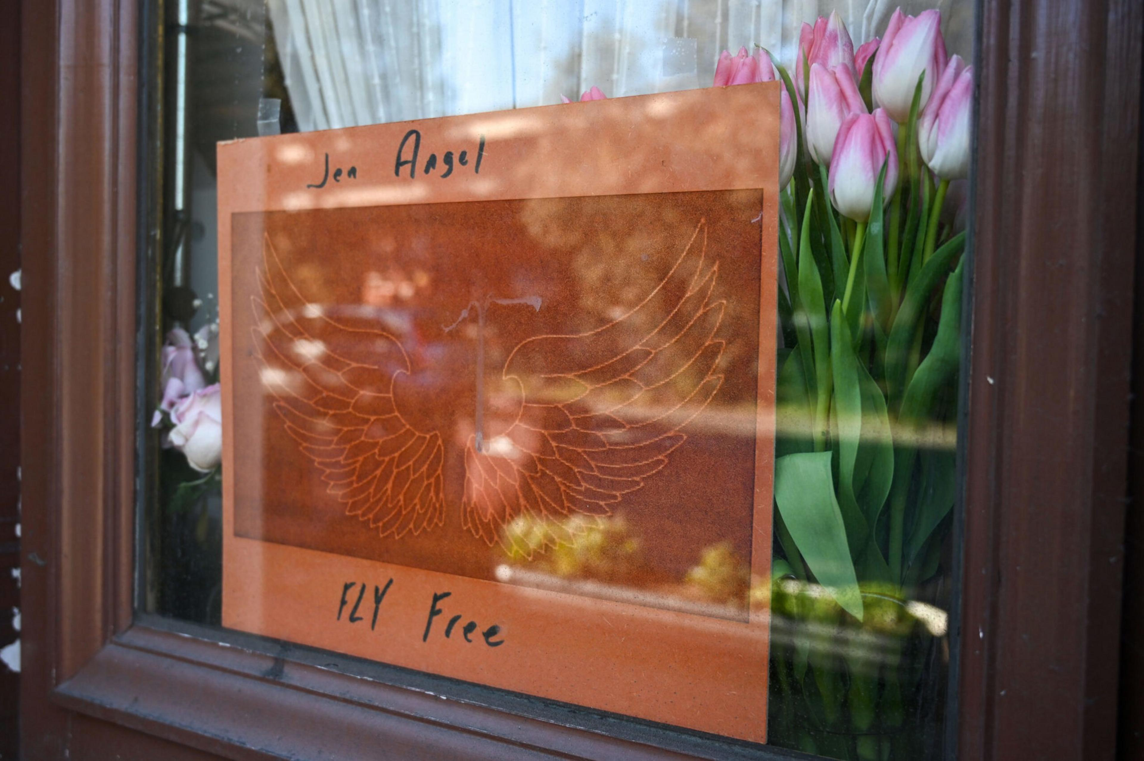 An orange card with engraved wings and the words "Jen Angel" and "FLY Free" is taped to a window beside a bouquet of pink tulips.