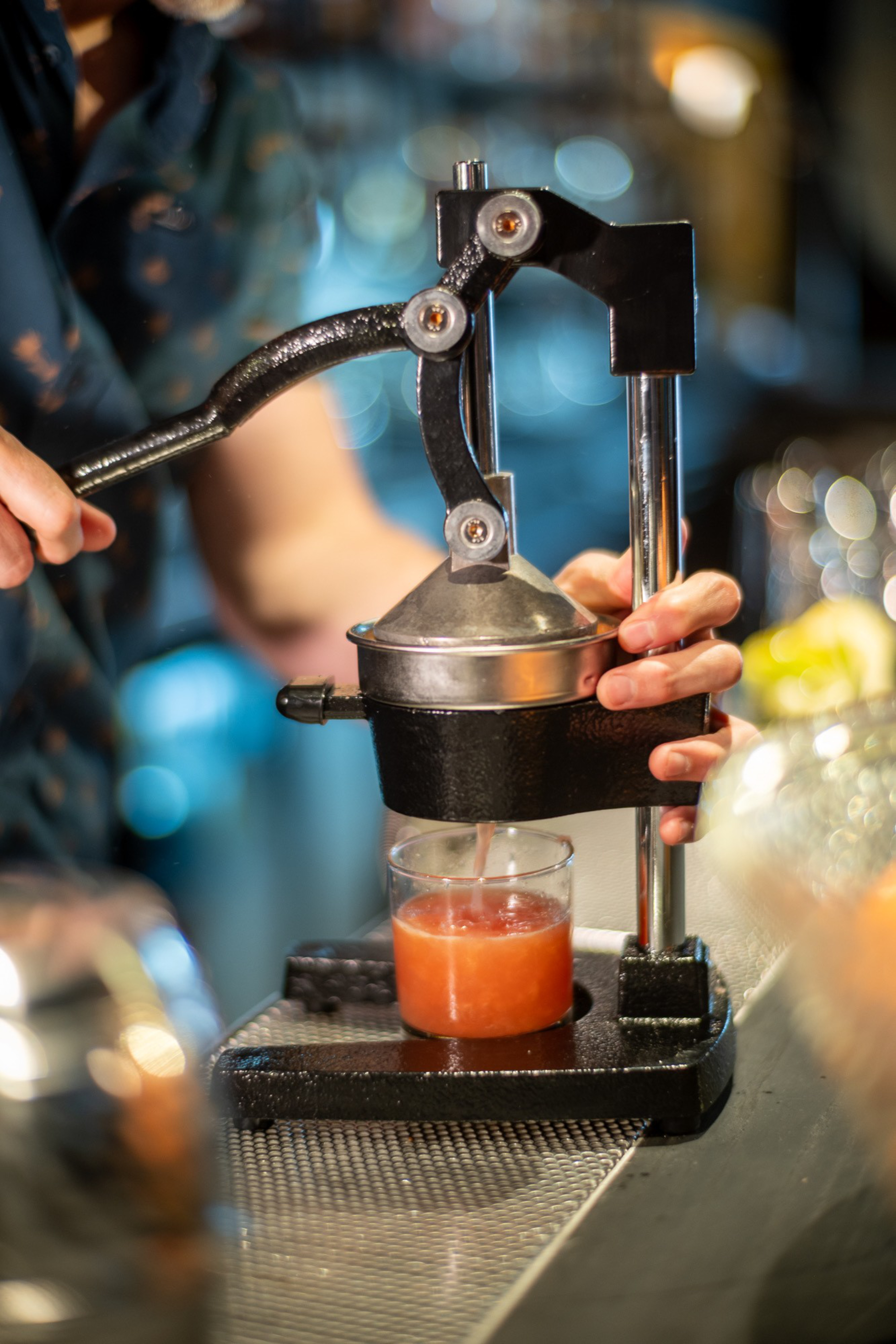 A person uses a manual citrus press to extract juice into a glass, with the juice flowing out as the handle is pushed down.