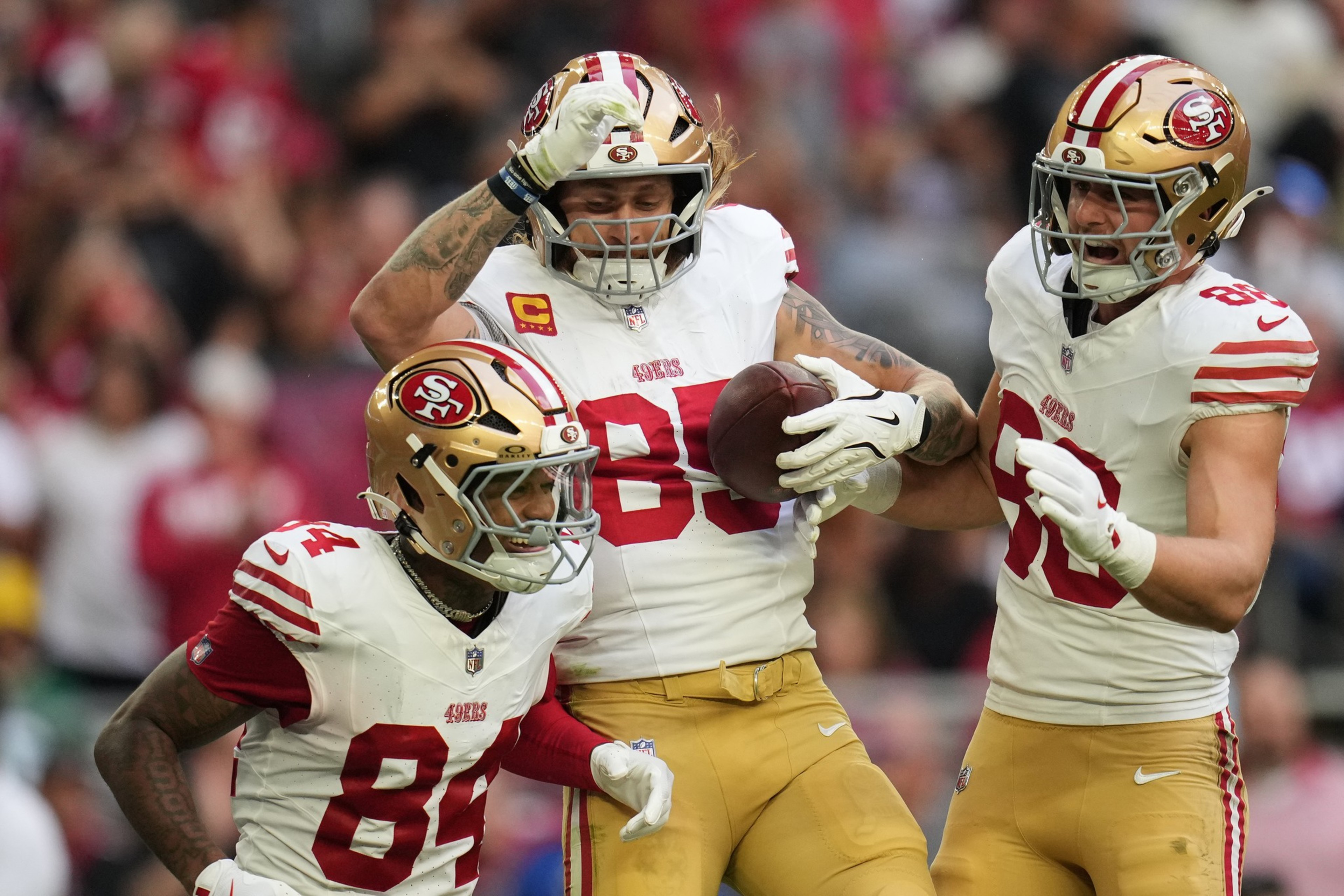 Three San Francisco 49ers football players celebrate, with one holding a football and two others raising their arms in excitement.
