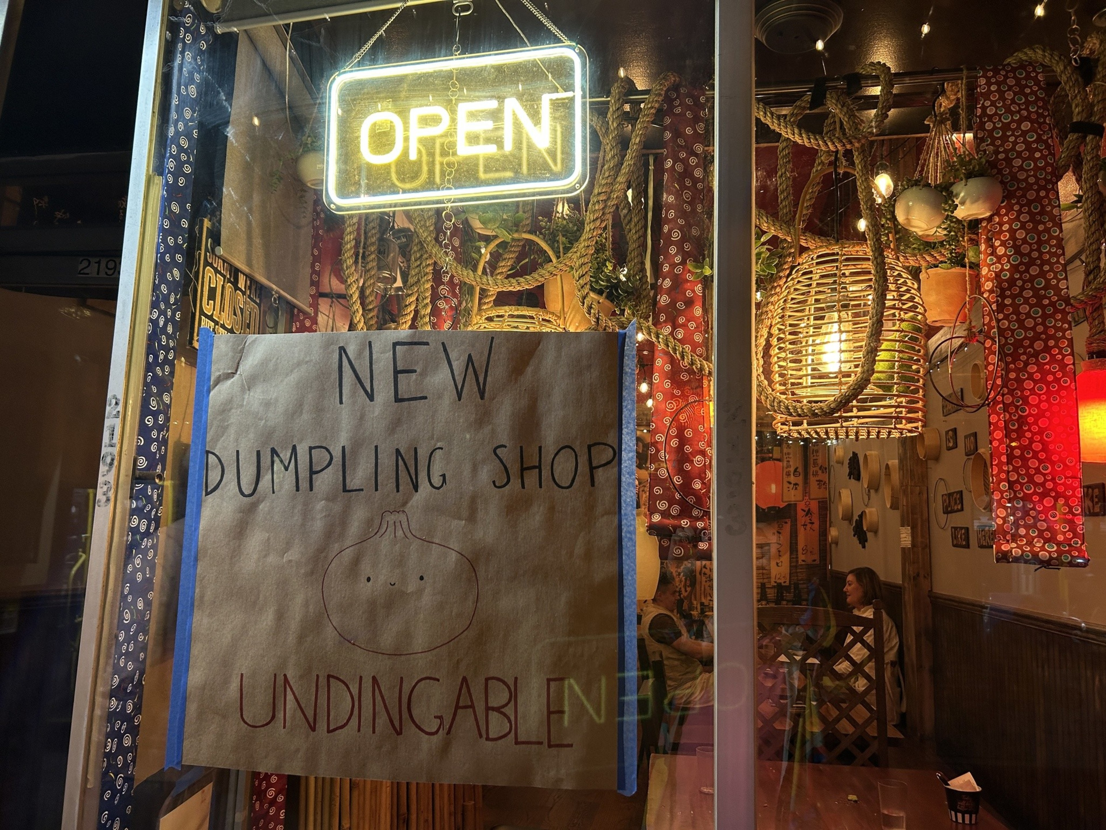 A neon 'open' sign is posted to the front door of a new restaurant in the Mission called Undingable, while diners sit in a homey interior.