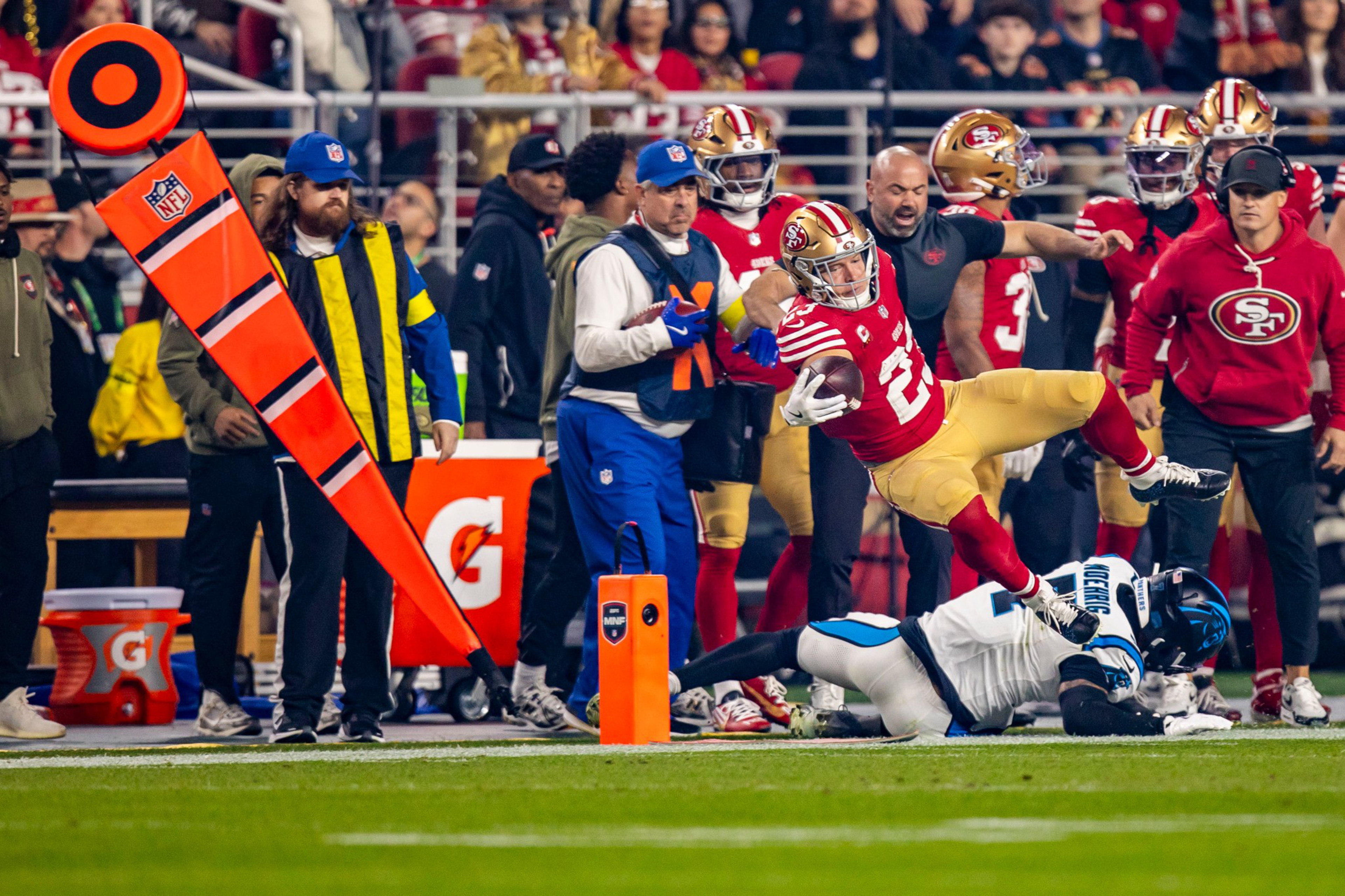 A San Francisco 49ers player leaps over a diving Carolina Panthers defender near the sideline during an intense football game.