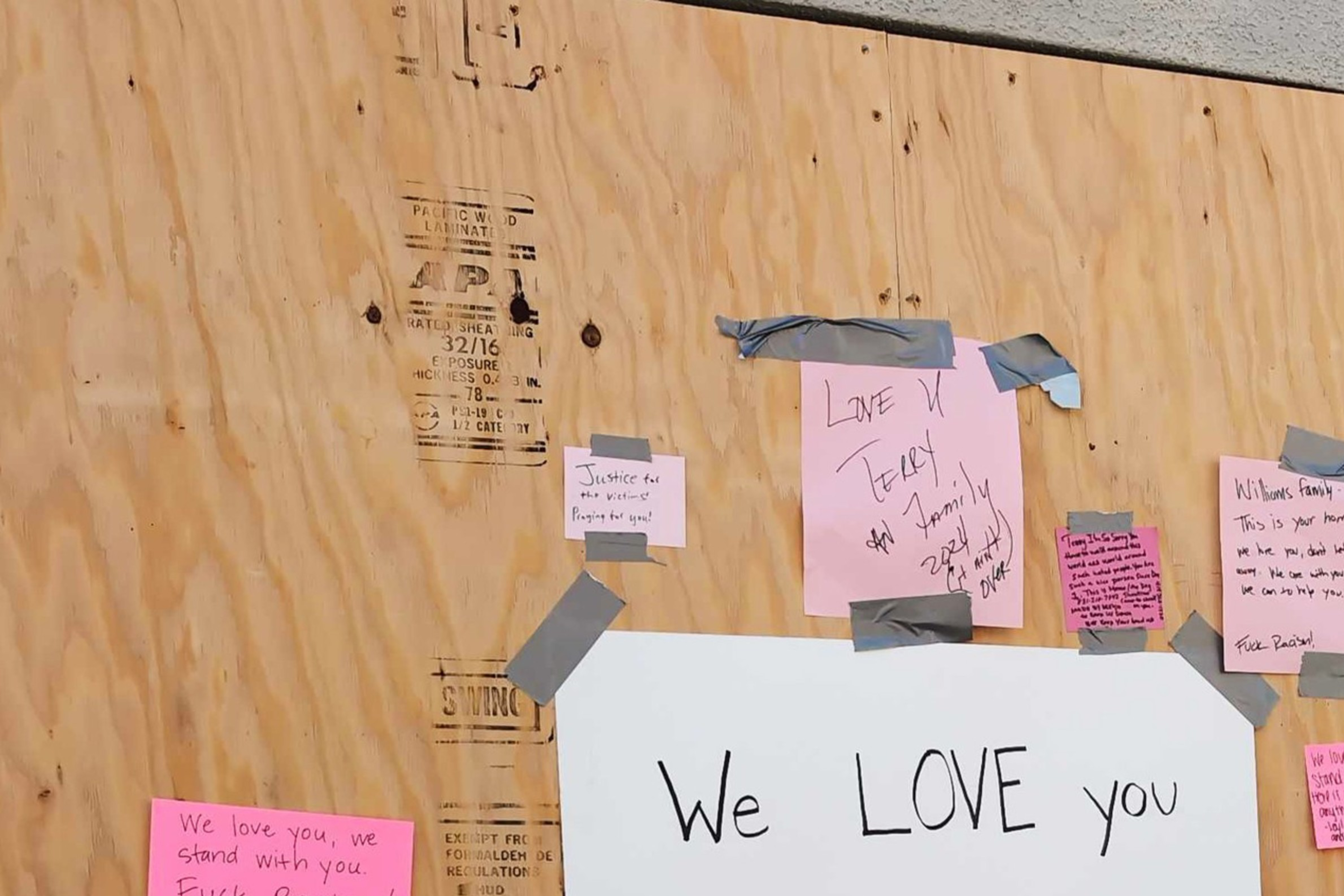 A plywood wall covered with various handwritten notes of support taped on. A large central sign reads, "We LOVE you WILLIAMS'."