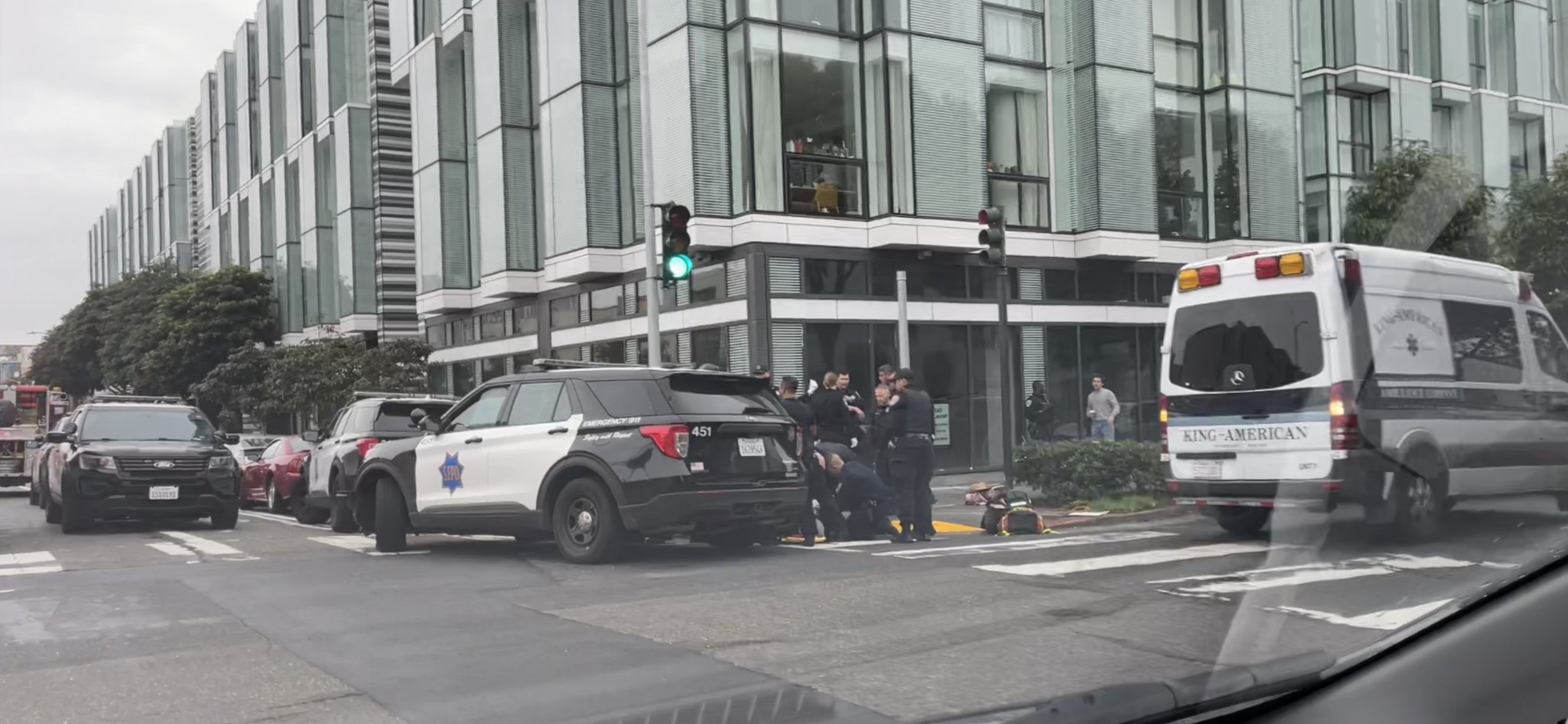 Police officers surround a stretcher on the ground as police cars, an ambulance and a fire engine are parked nearby.