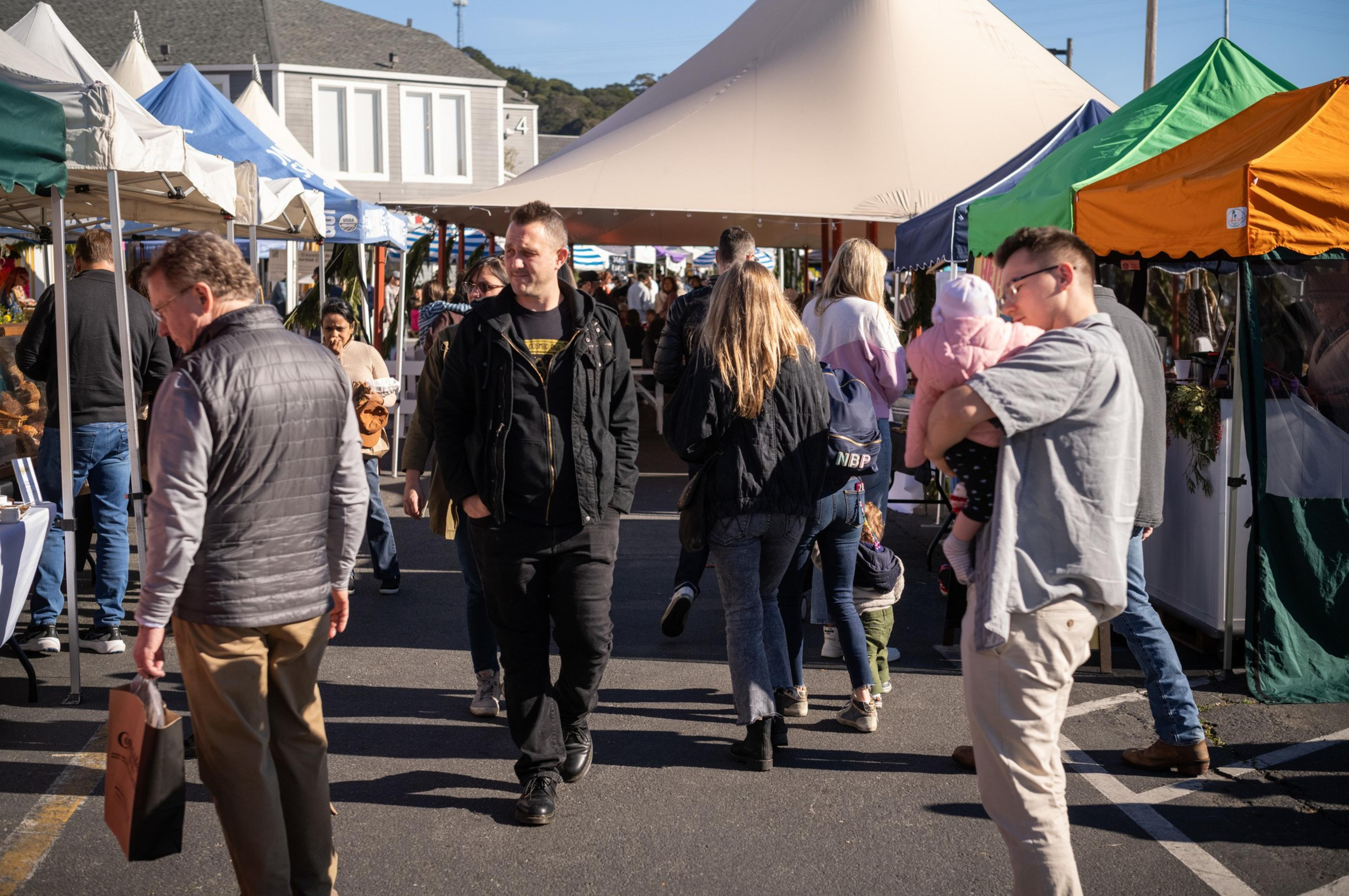 a crowd of people shopping nera farmers market tents on a sunny day