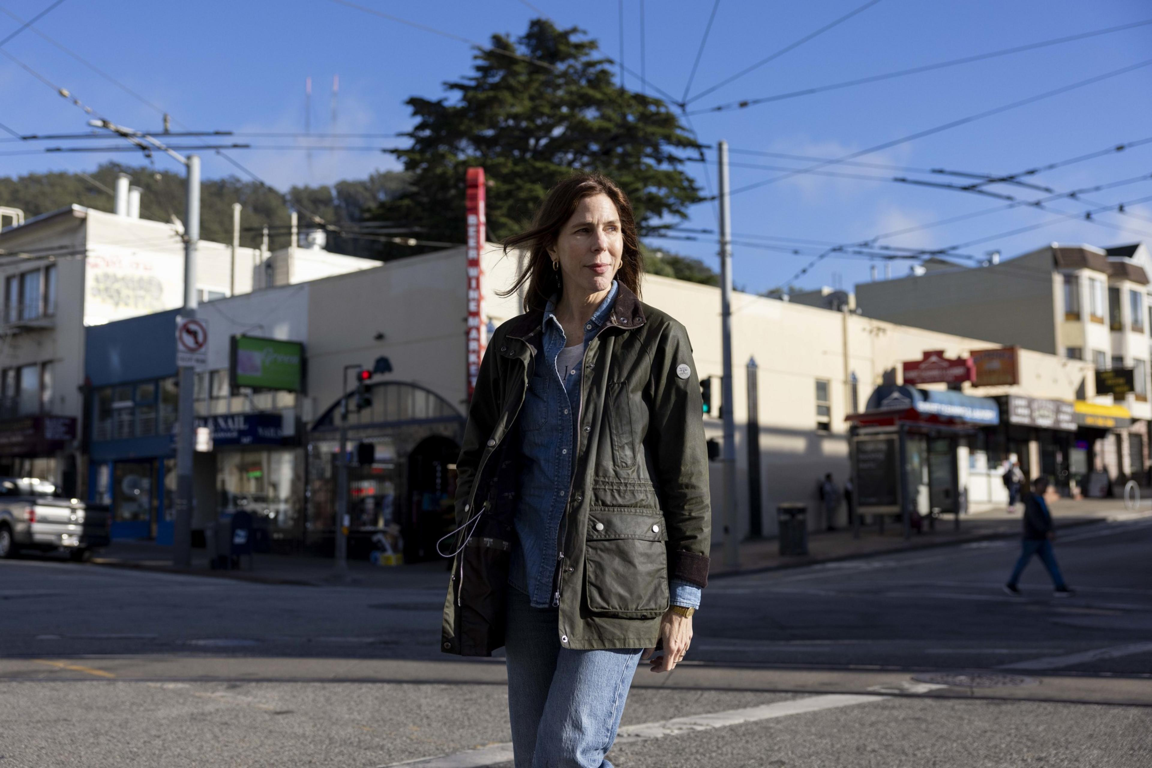 A woman in a green jacket walks across the street.