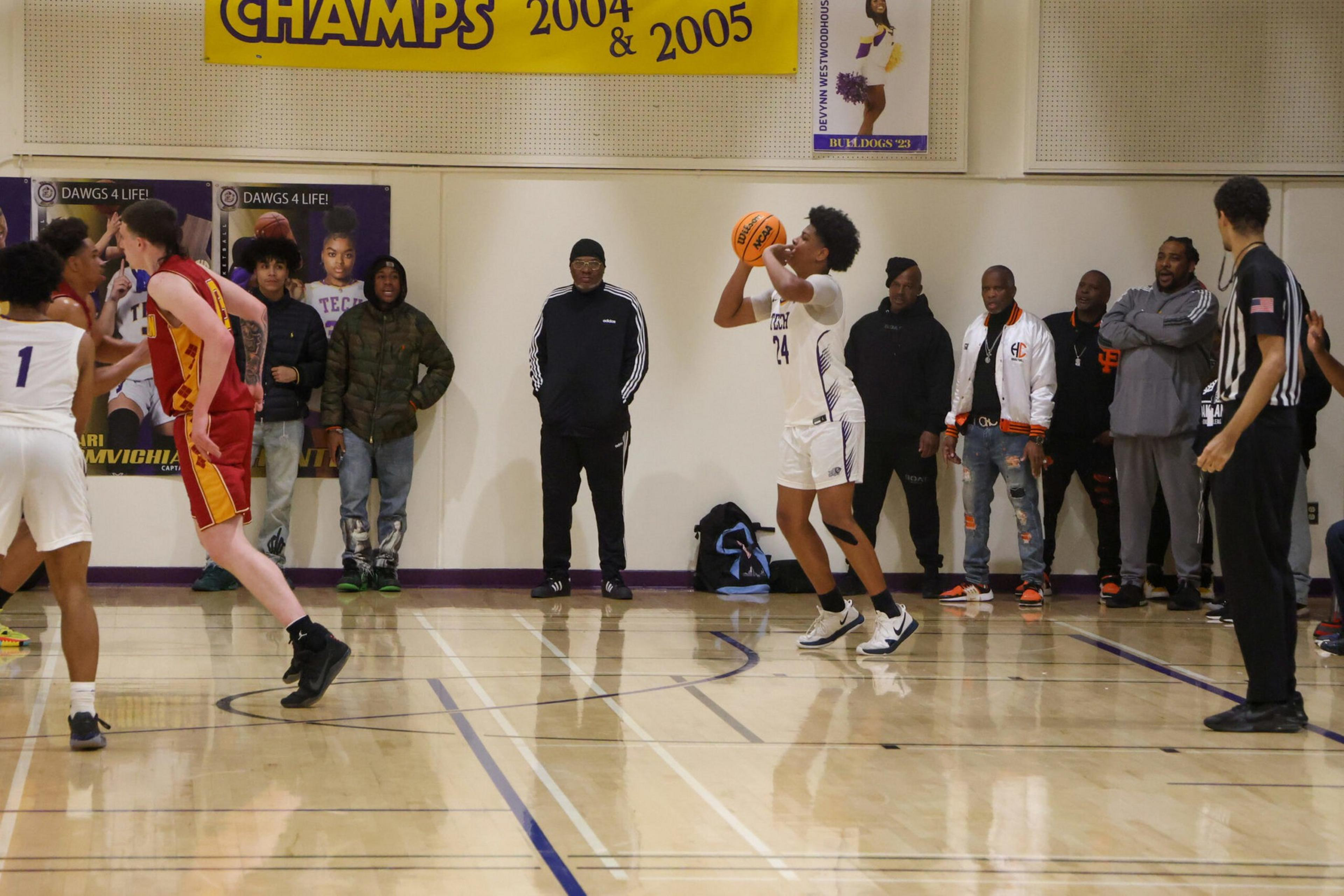 A basketball player in a white uniform prepares to shoot while opponents, spectators, and a referee watch from the court and sidelines.
