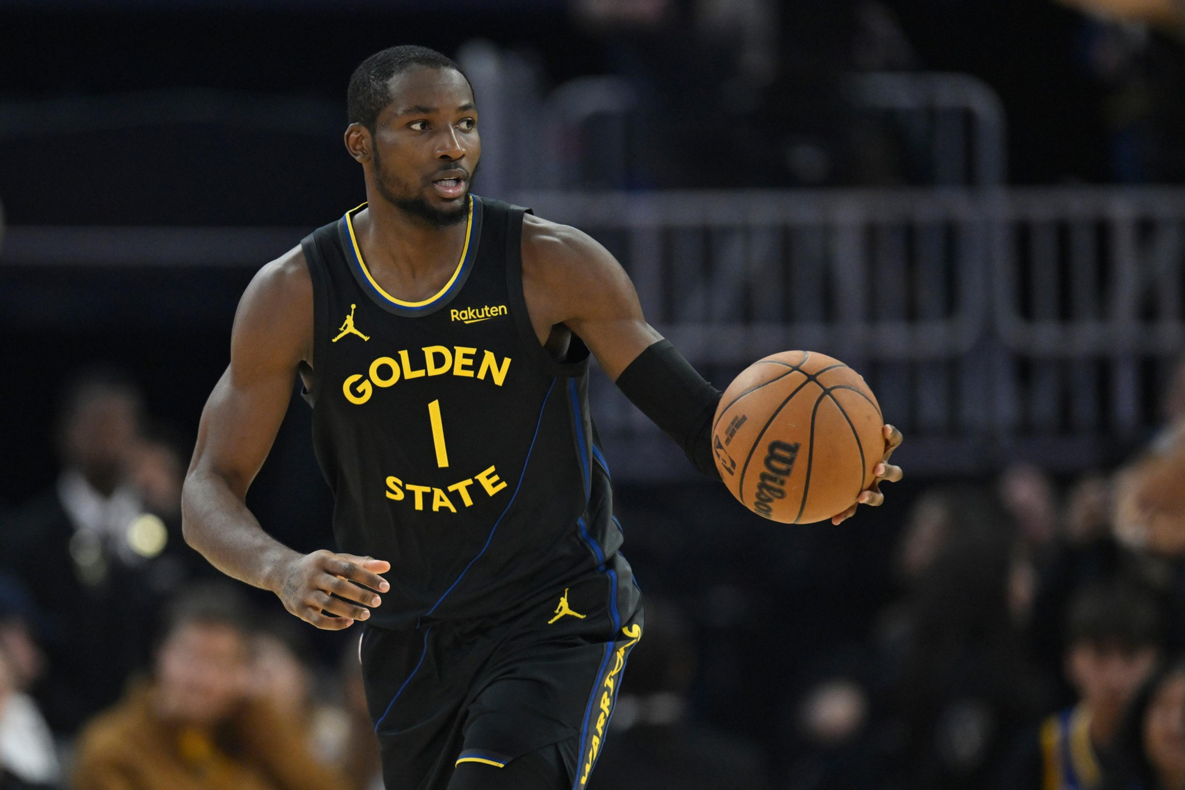 A basketball player in a black Golden State Warriors uniform dribbles the ball, looking to his left during a game.