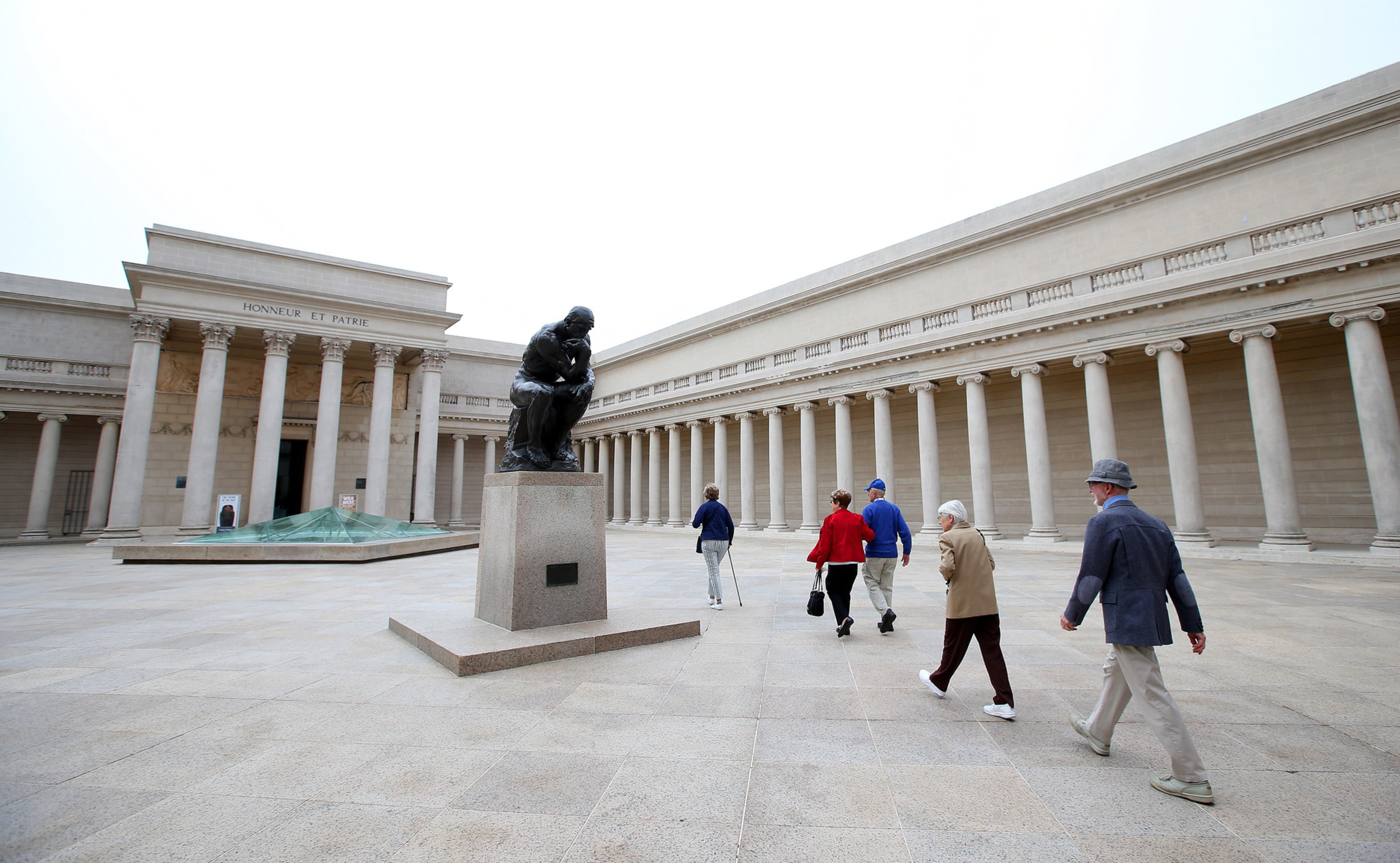 Visitors walk by a statue in front of a building with classical columns and the inscription "HONNEUR ET PATRIE."