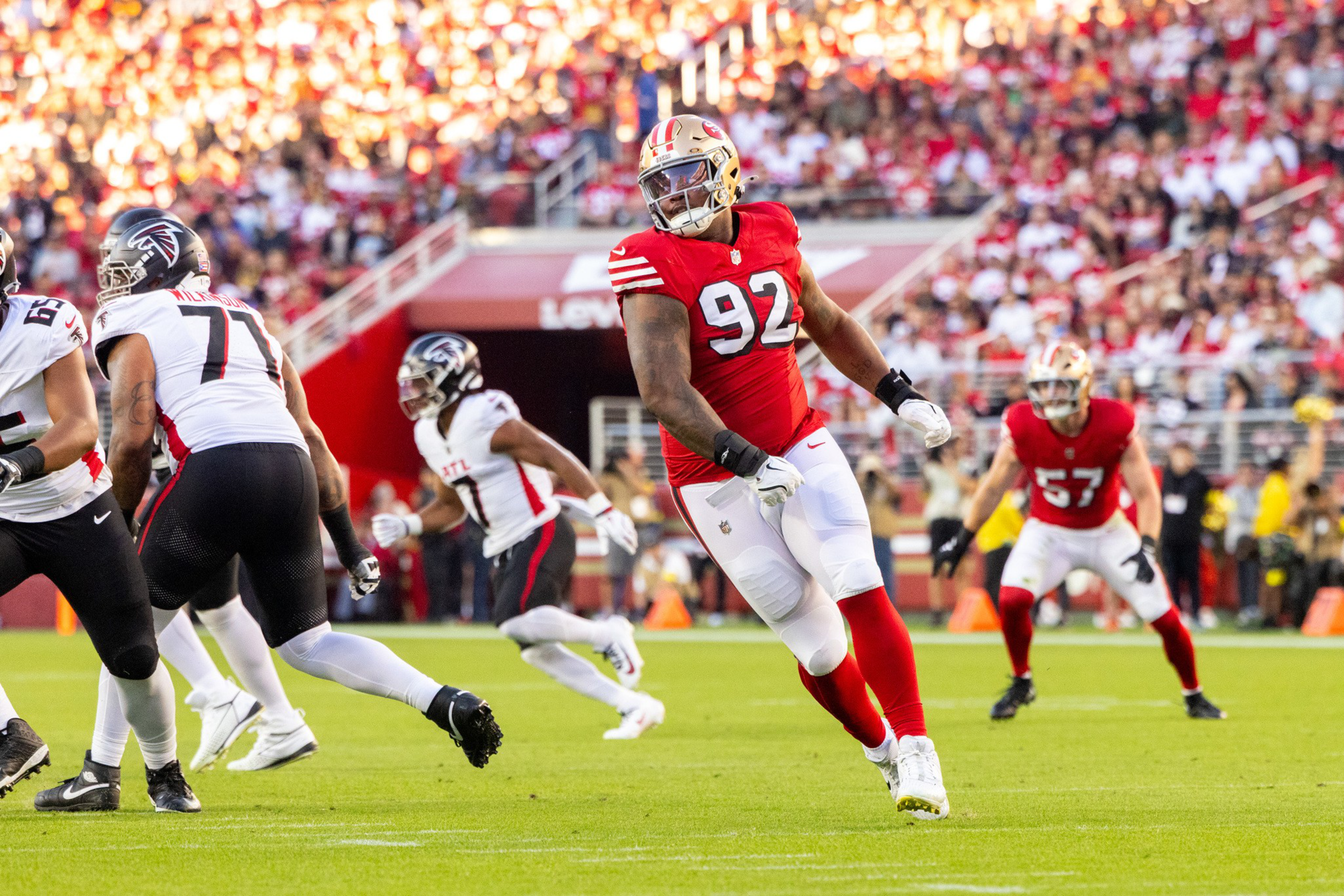 A football player in a red jersey with number 92 is running on the field while players in white jerseys from the opposing team prepare to block or run.