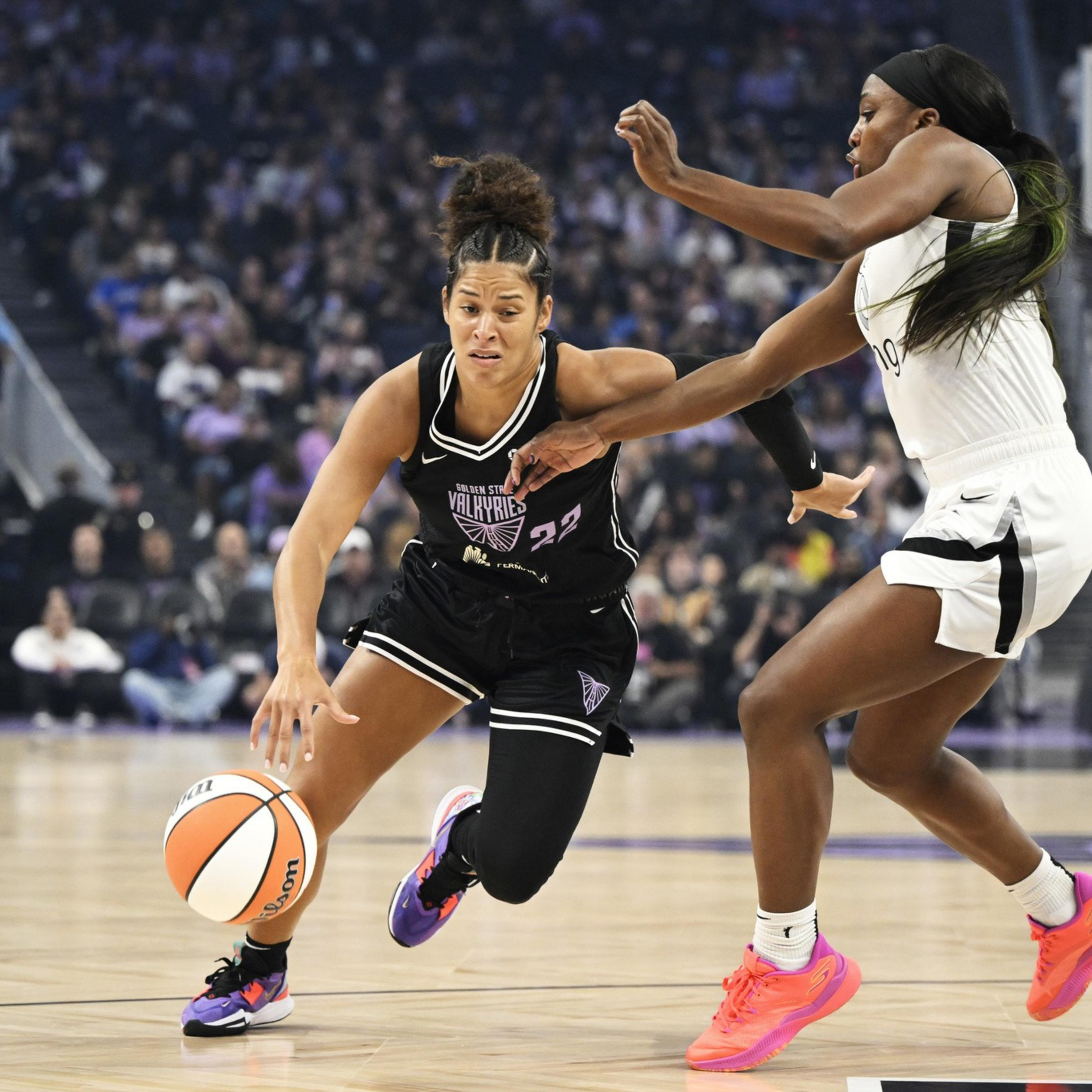 A basketball player in a black jersey dribbles the ball while being closely guarded by a player in a white jersey during a game.