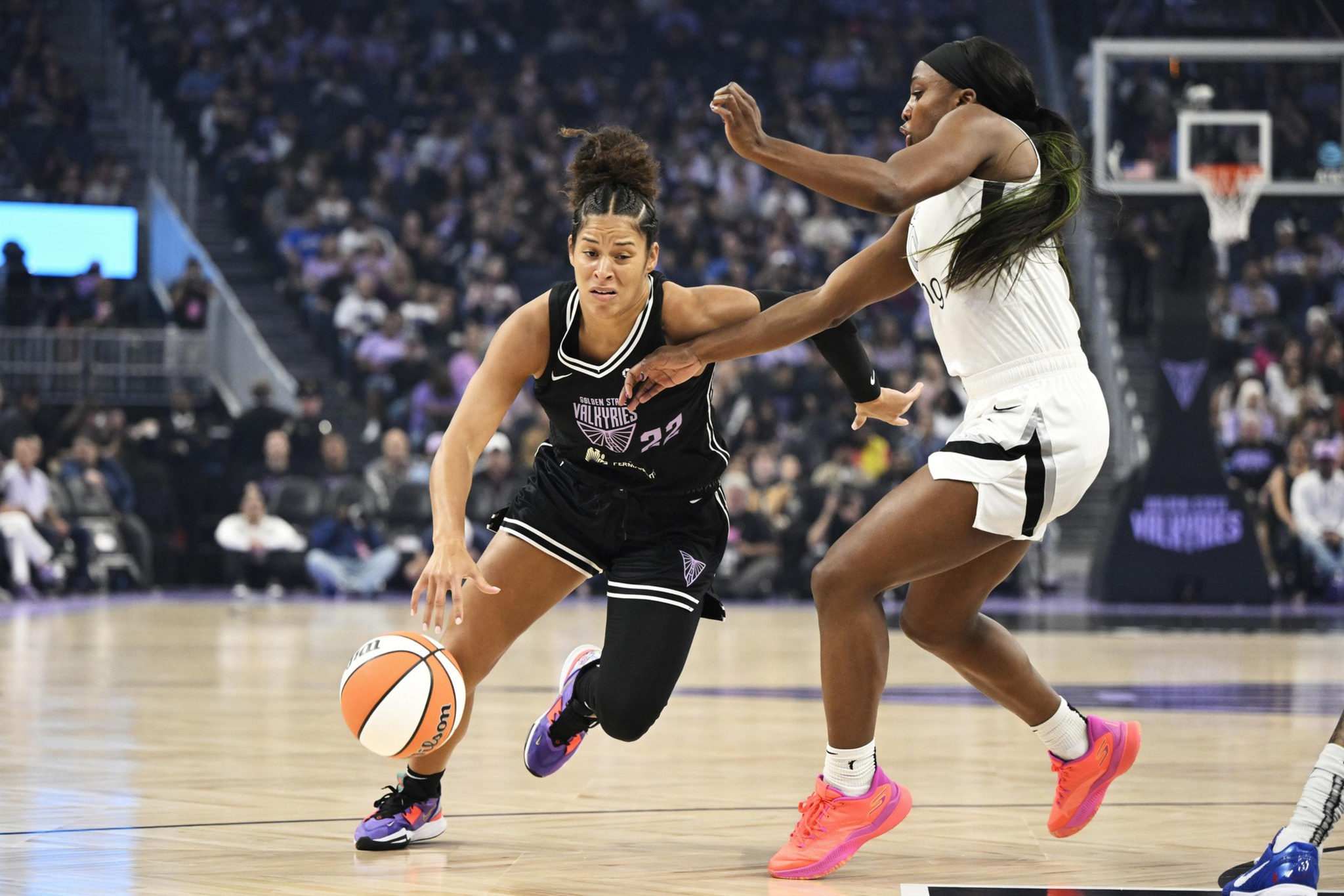 A basketball player in a black jersey dribbles the ball while being closely guarded by a player in a white jersey during a game.