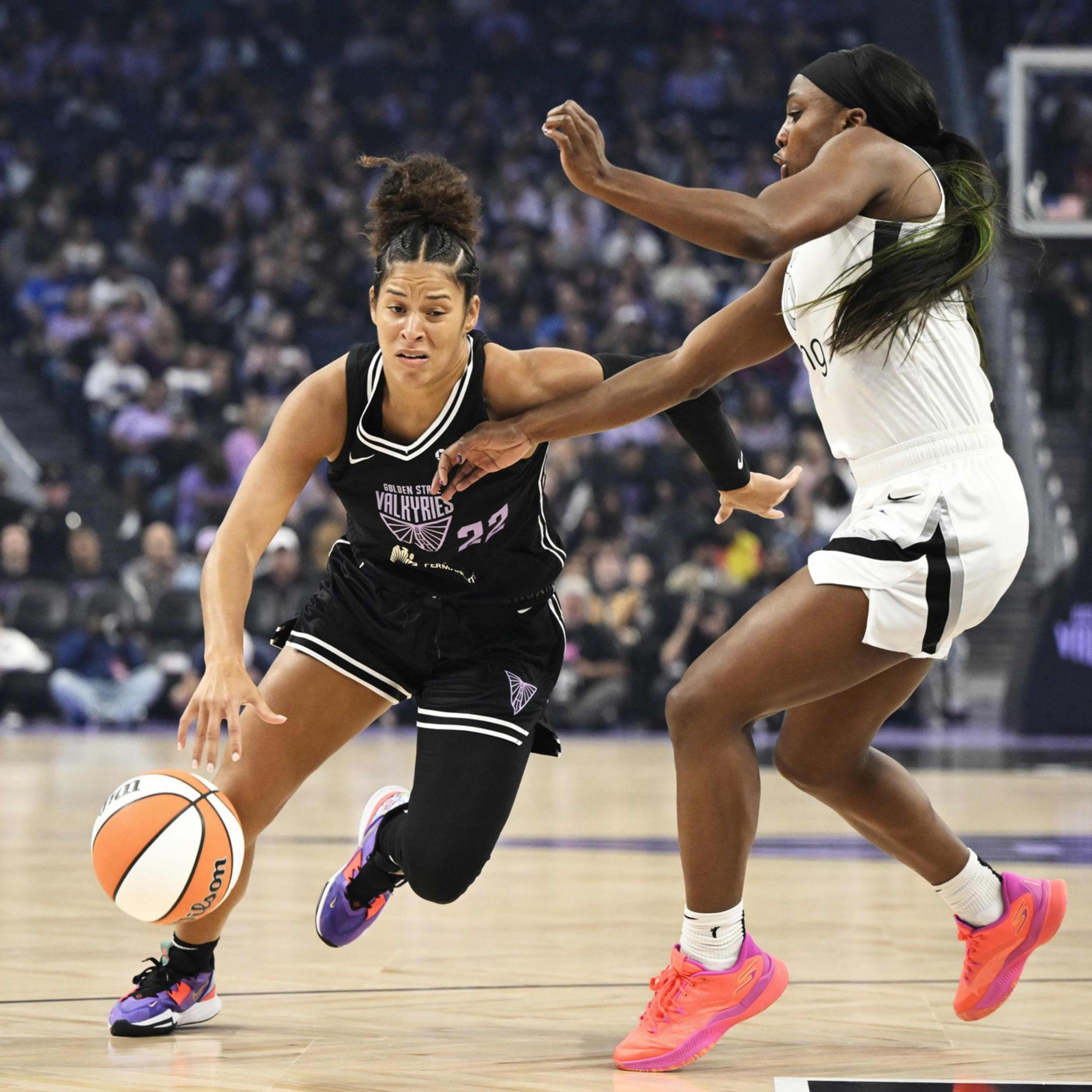 A basketball player in a black jersey dribbles the ball while being closely guarded by a player in a white jersey during a game.
