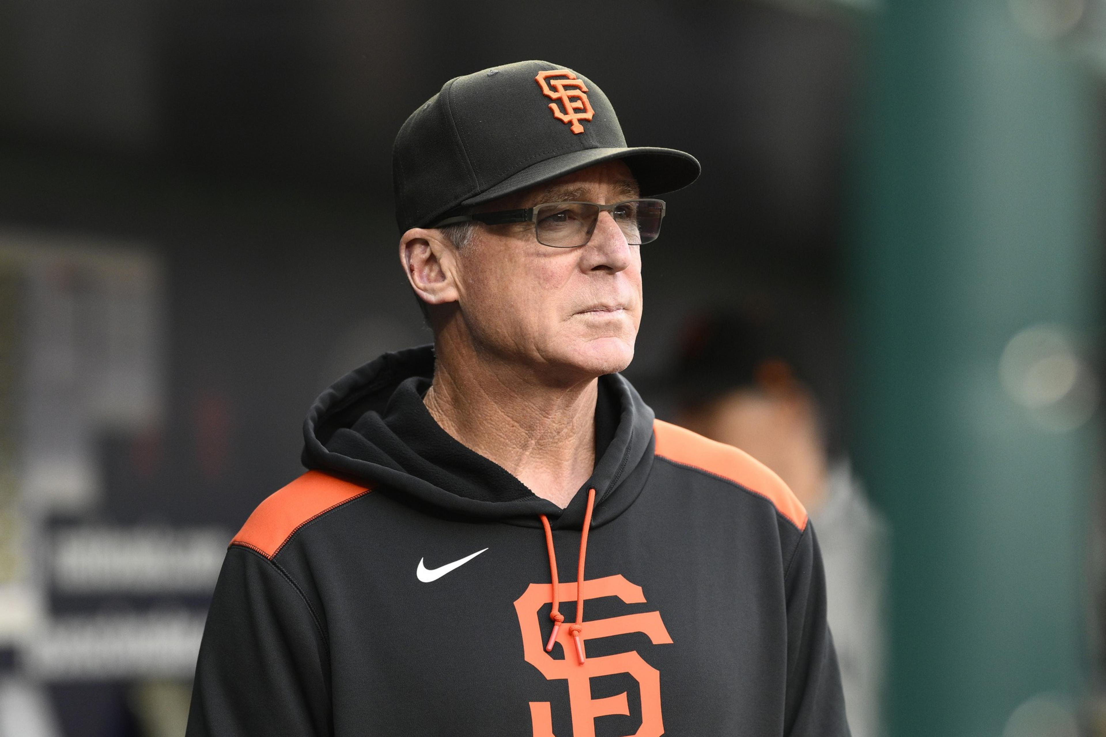 A man in a black hoodie and cap with an "SF" logo stands in focus, looking serious, with a blurred background.