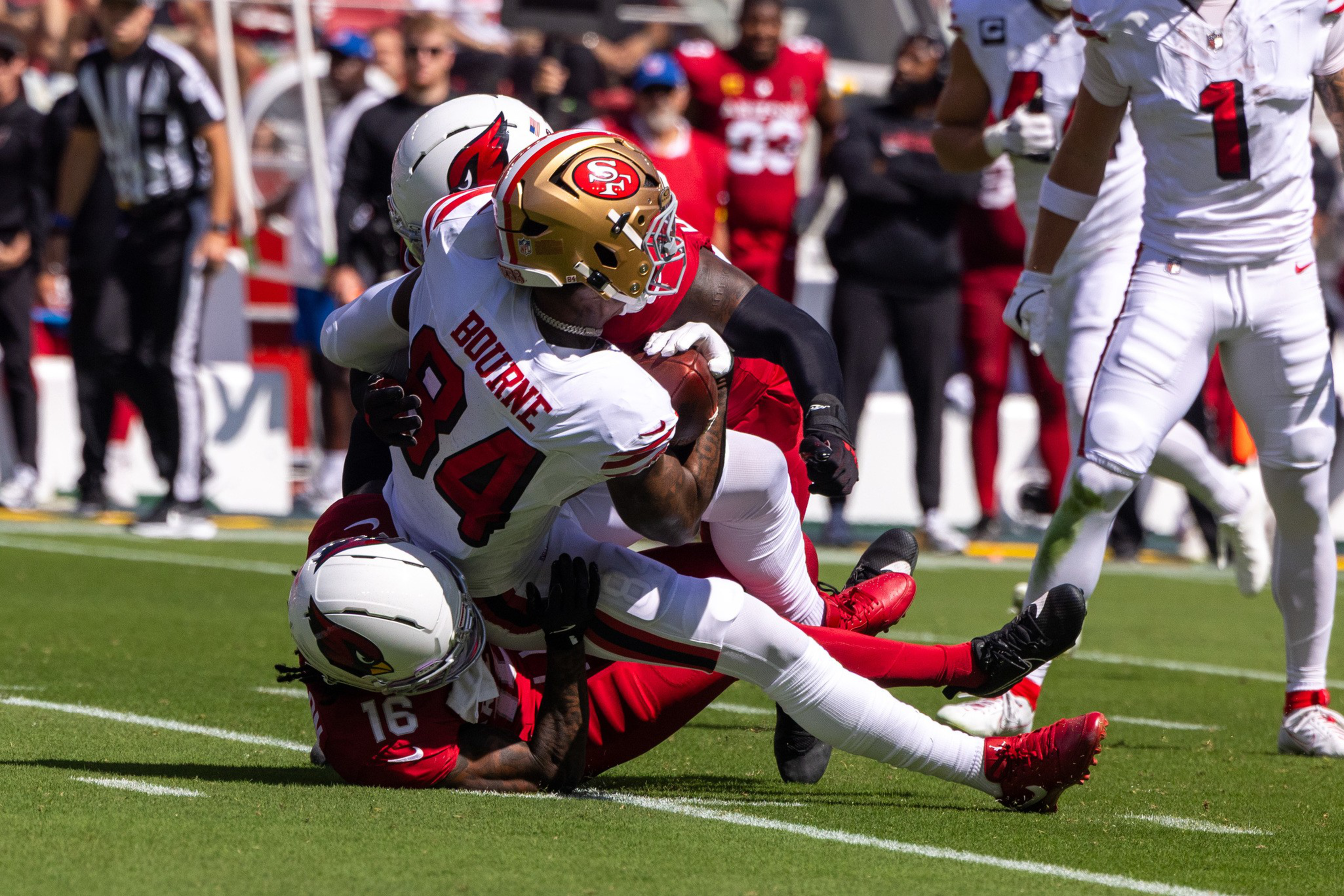 A football player in a white jersey with “Bourne” and number 84 tackles a player in a red jersey on a grassy field during a game.