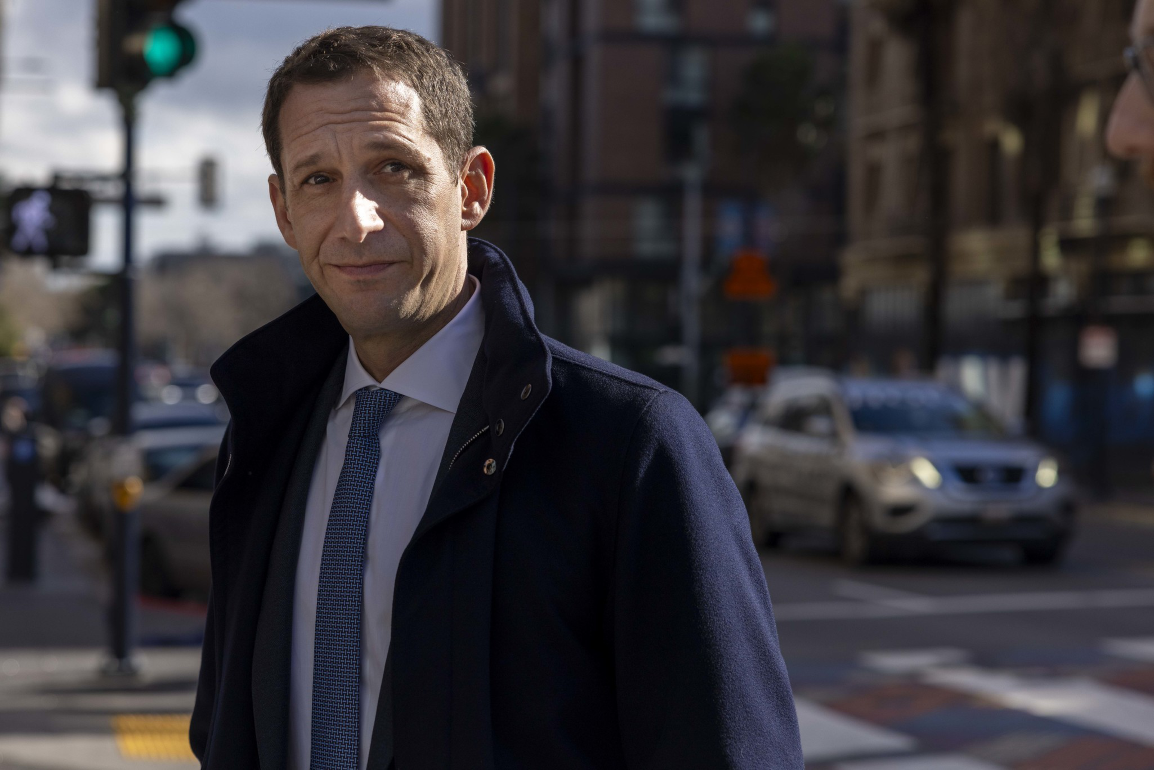 Mayor Daniel Lurie in a coat standing at an intersection.