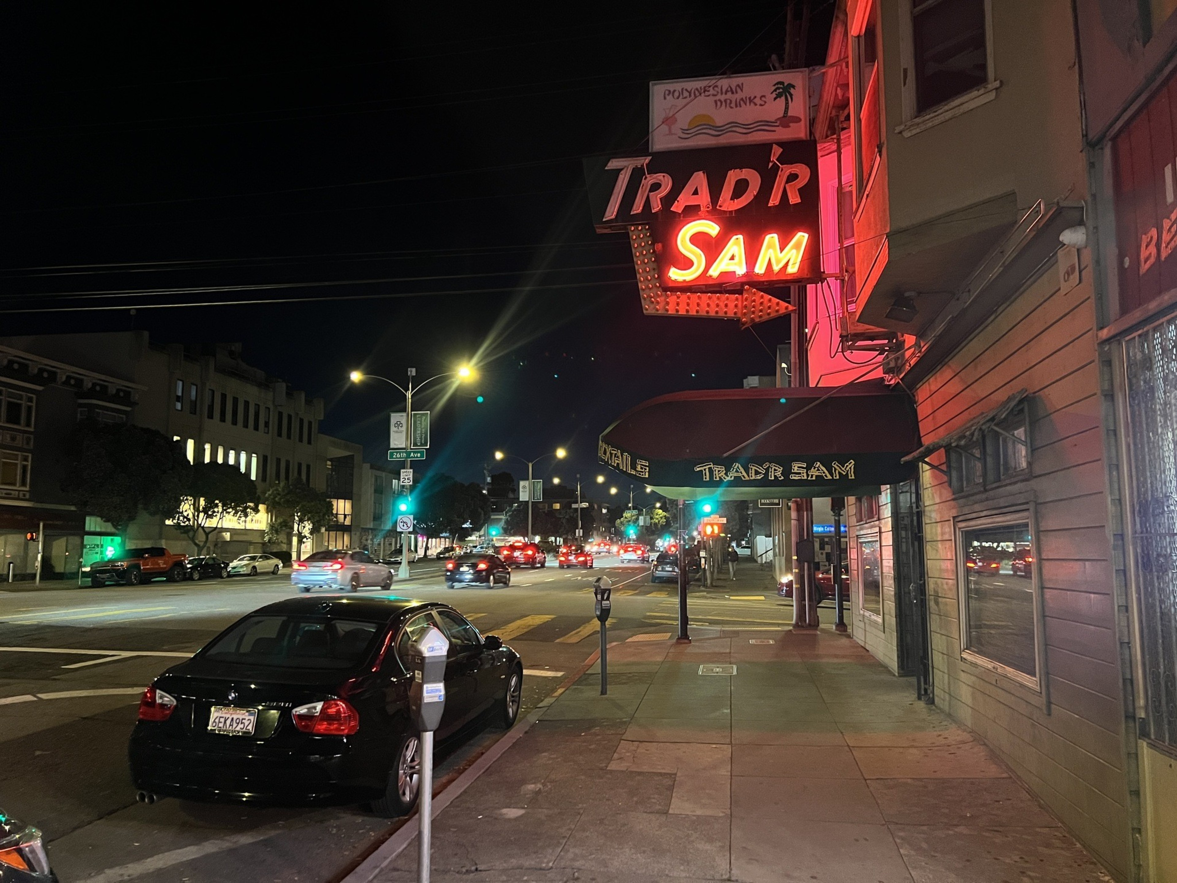 A neon sign reads "Sam" on a city street in San Francisco at night.