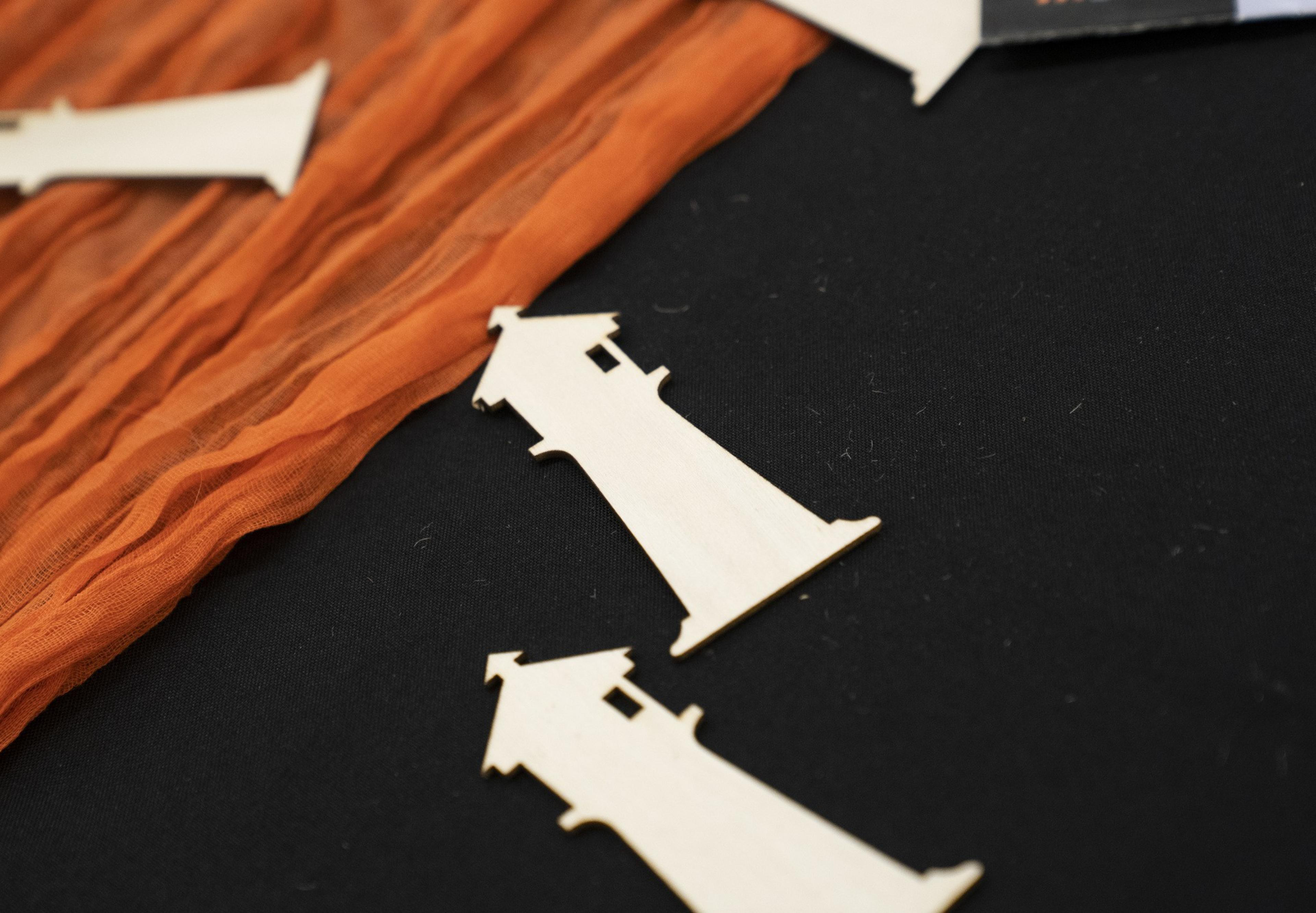 Wooden lighthouse cutouts lie on a black surface, with an orange textured fabric draped in the background.