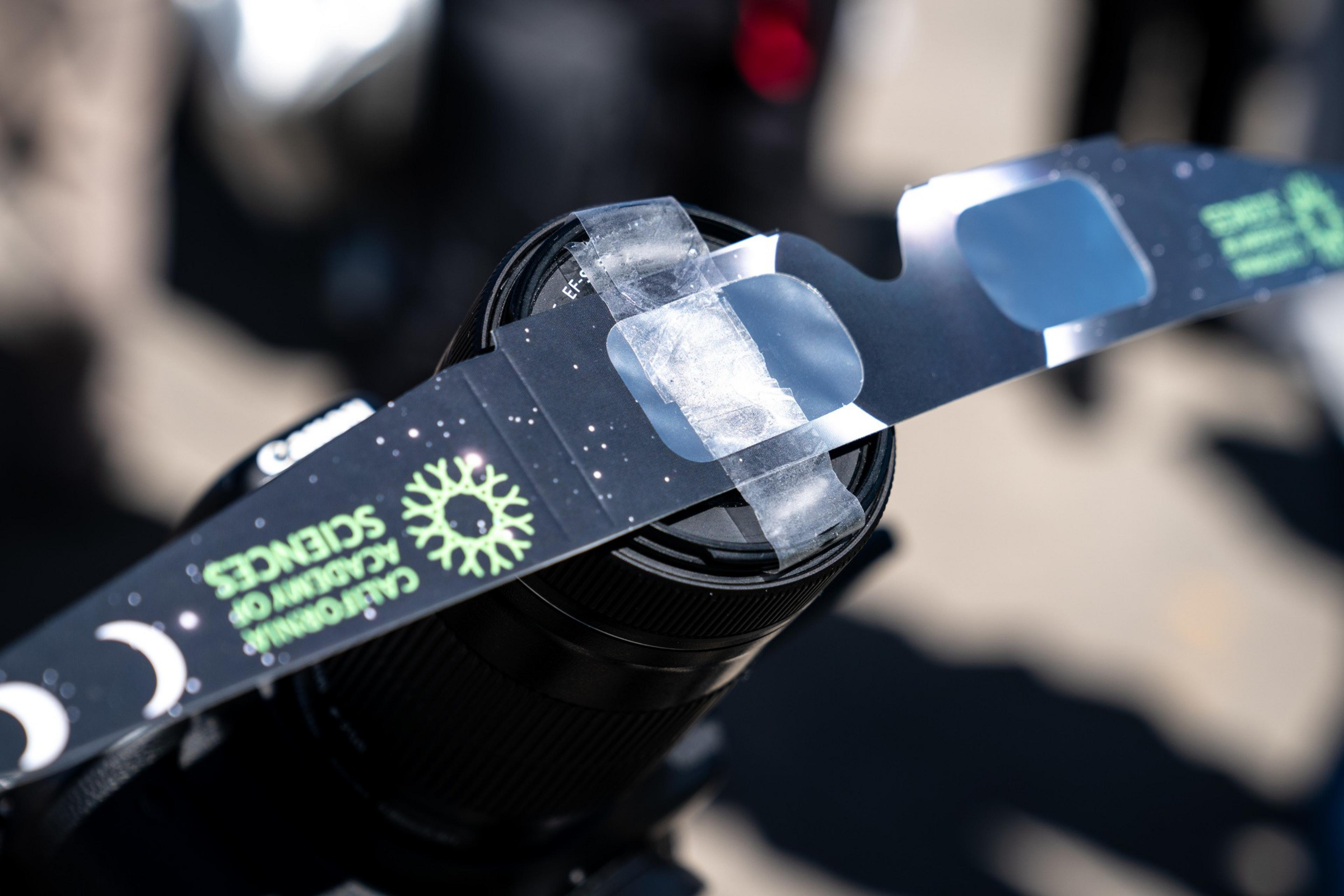 A camera lens with a DIY solar eclipse filter made of cardboard and ice.