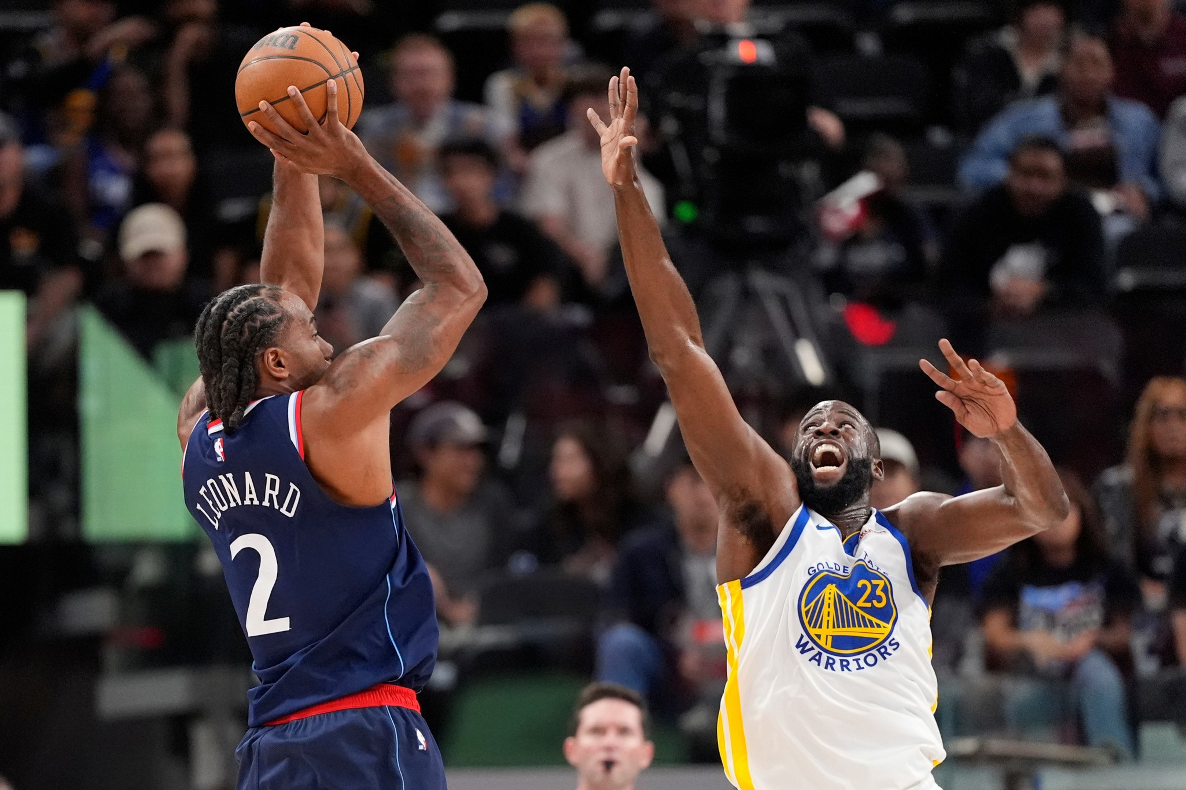 Kawhi Leonard of the Clippers jumps to shoot as Draymond Green of the Warriors raises his arms to block during a basketball game.