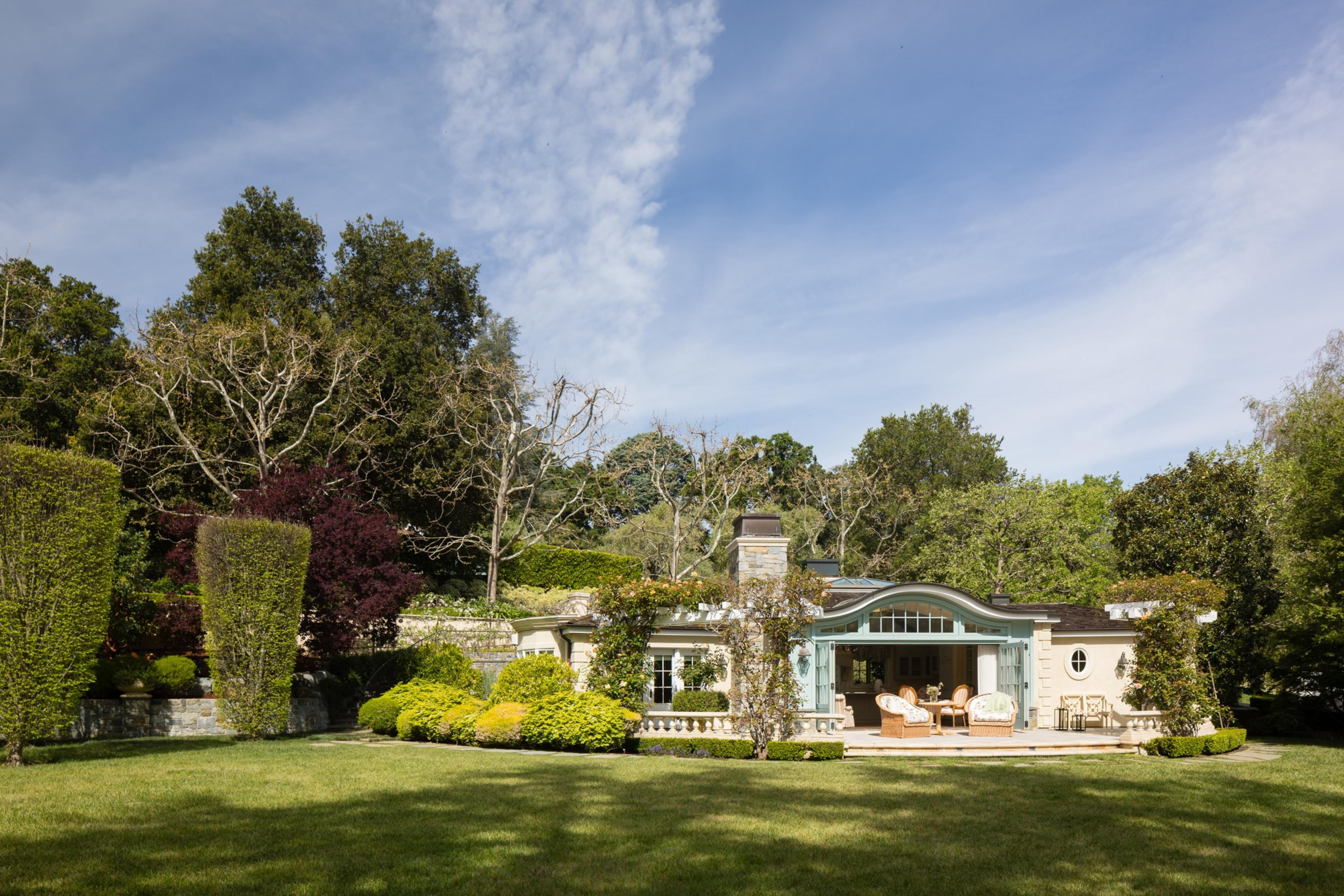 A serene backyard with a lush lawn, manicured hedges, colorful trees, and a cozy house with a patio.