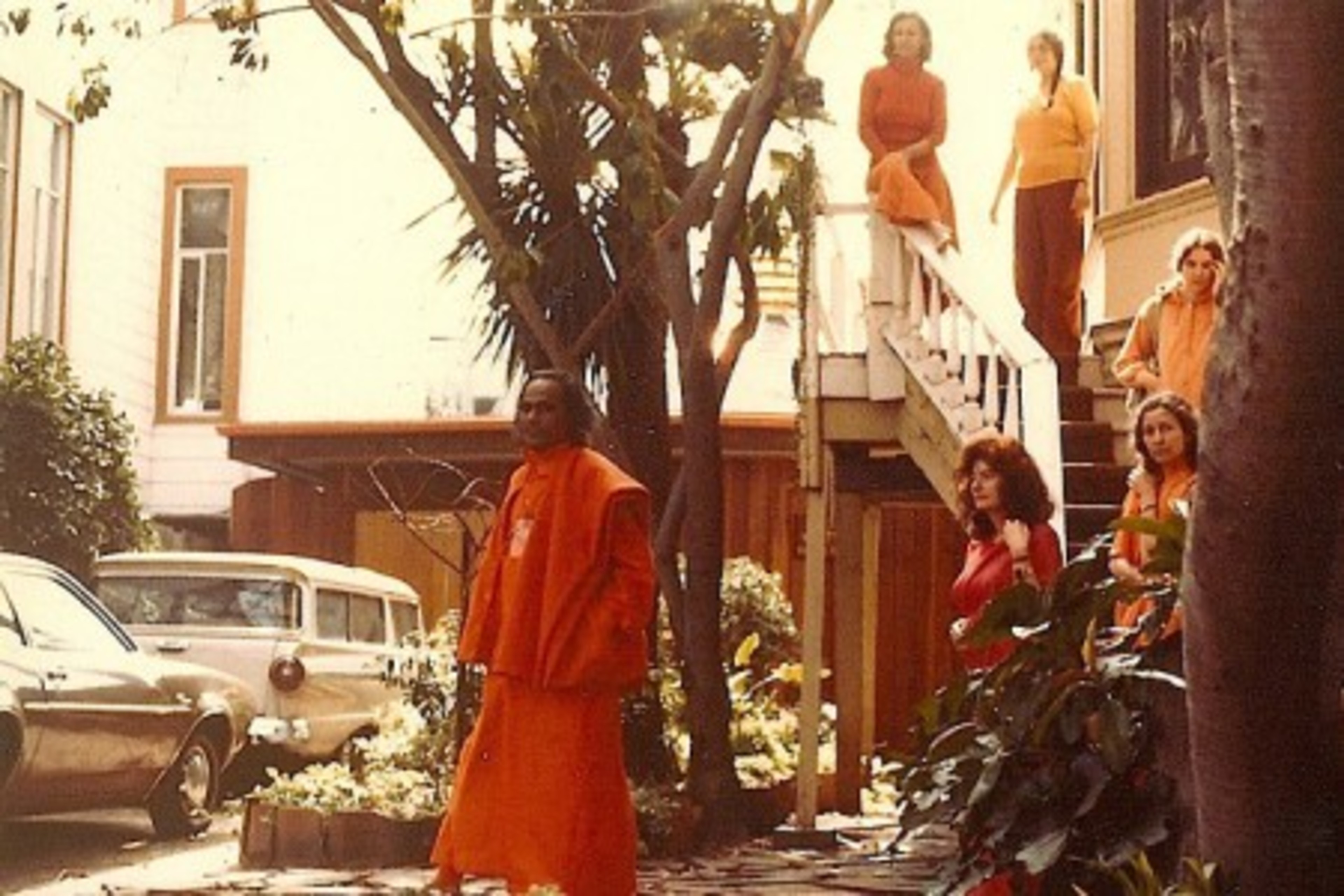 A man in orange walks in front of steps with five people in orange following behind him.