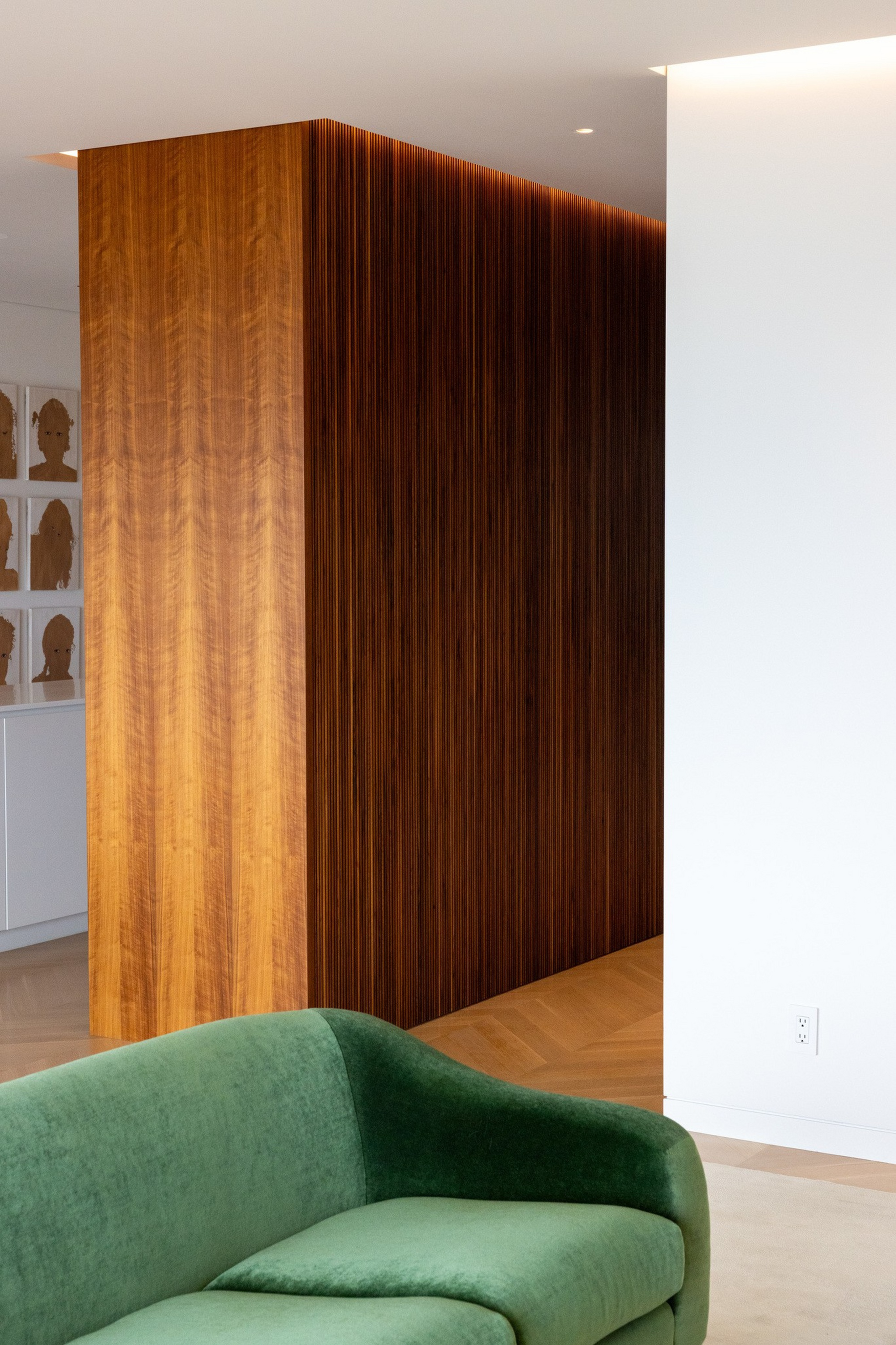 A green velvet sofa sits near a corner with warm wooden paneling and white walls, creating a modern and cozy interior space.