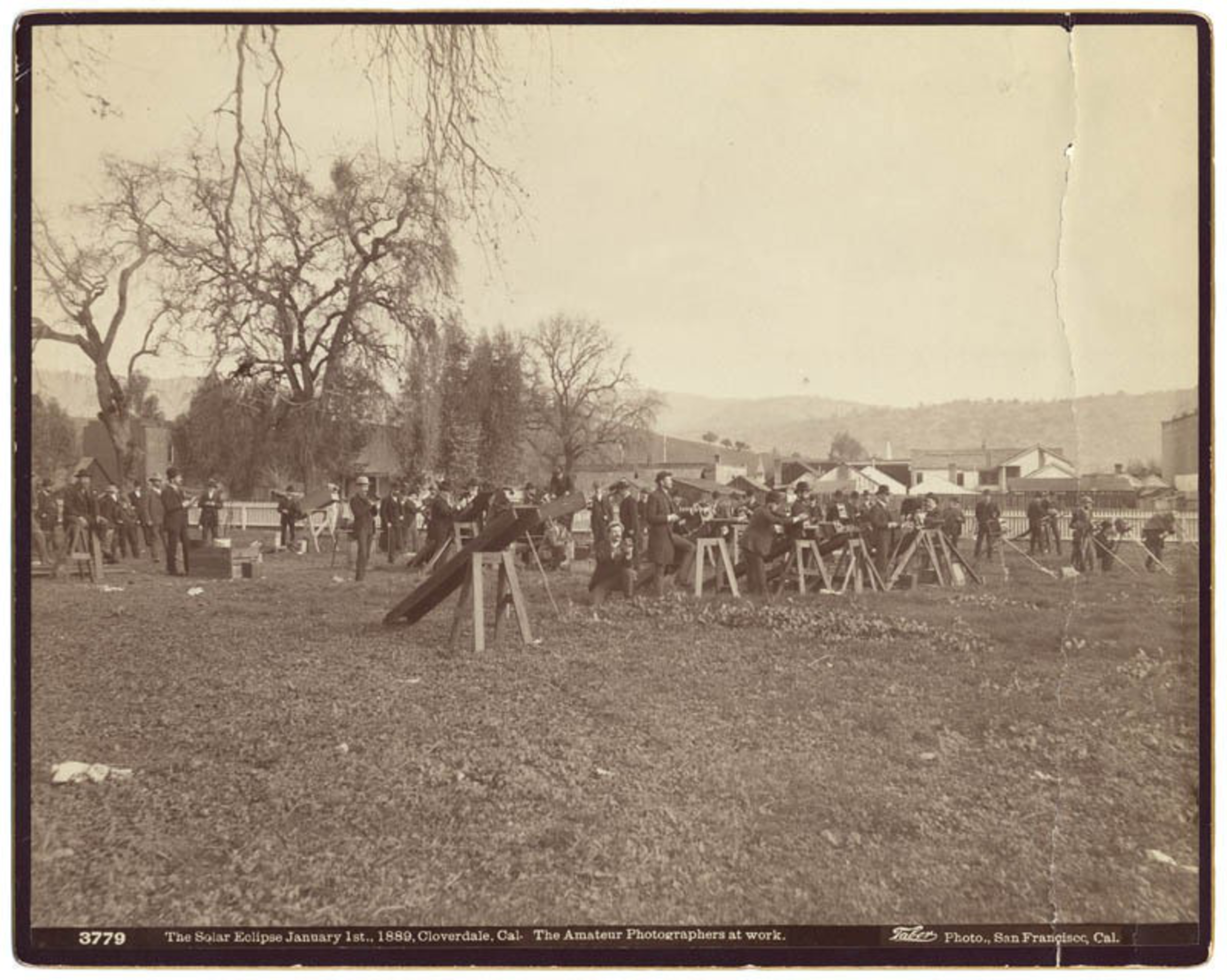 A vintage photo of people with cameras on tripods outdoors, observing a solar eclipse.