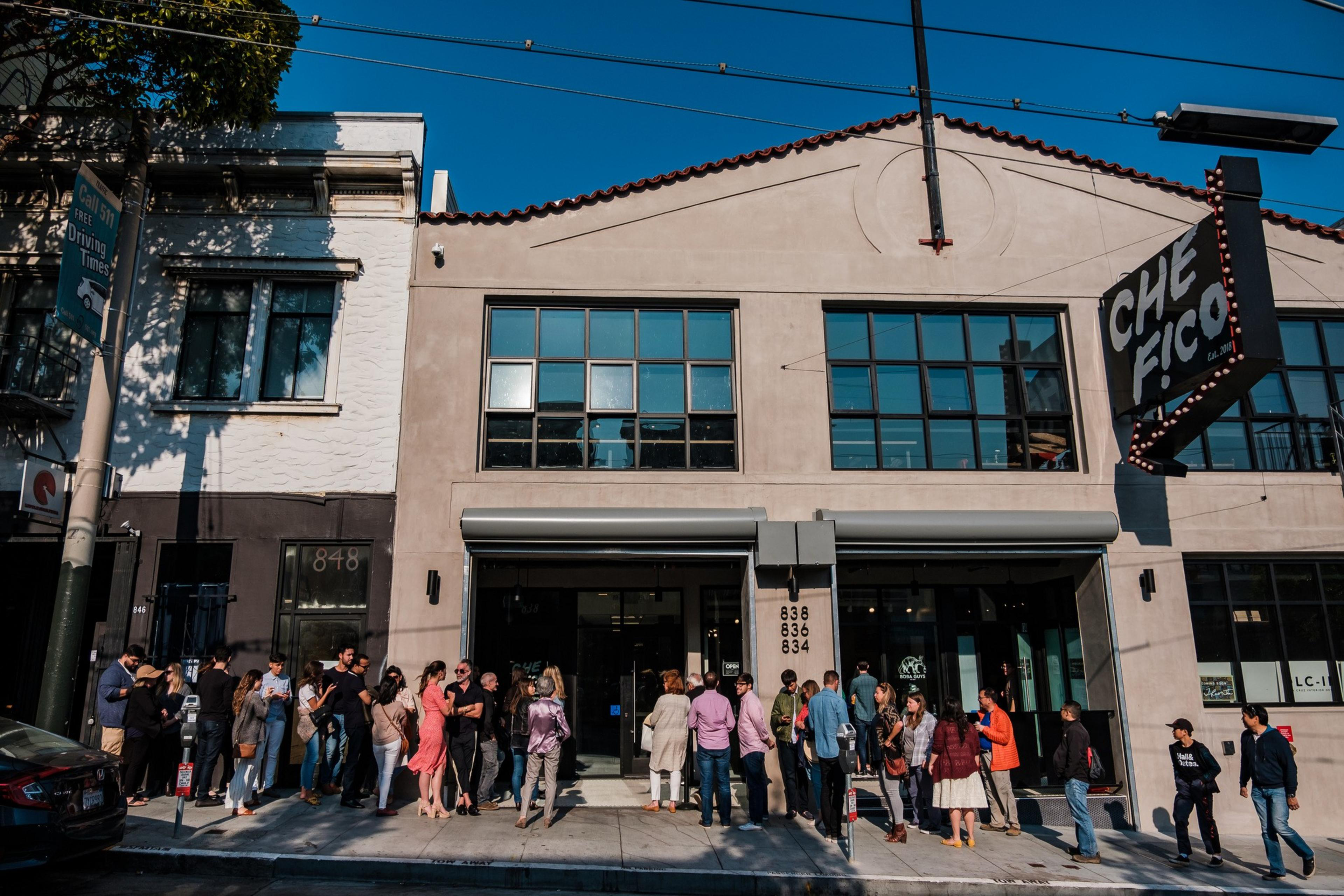 People queue outside &quot;Che Fico&quot; restaurant on a sunny day.