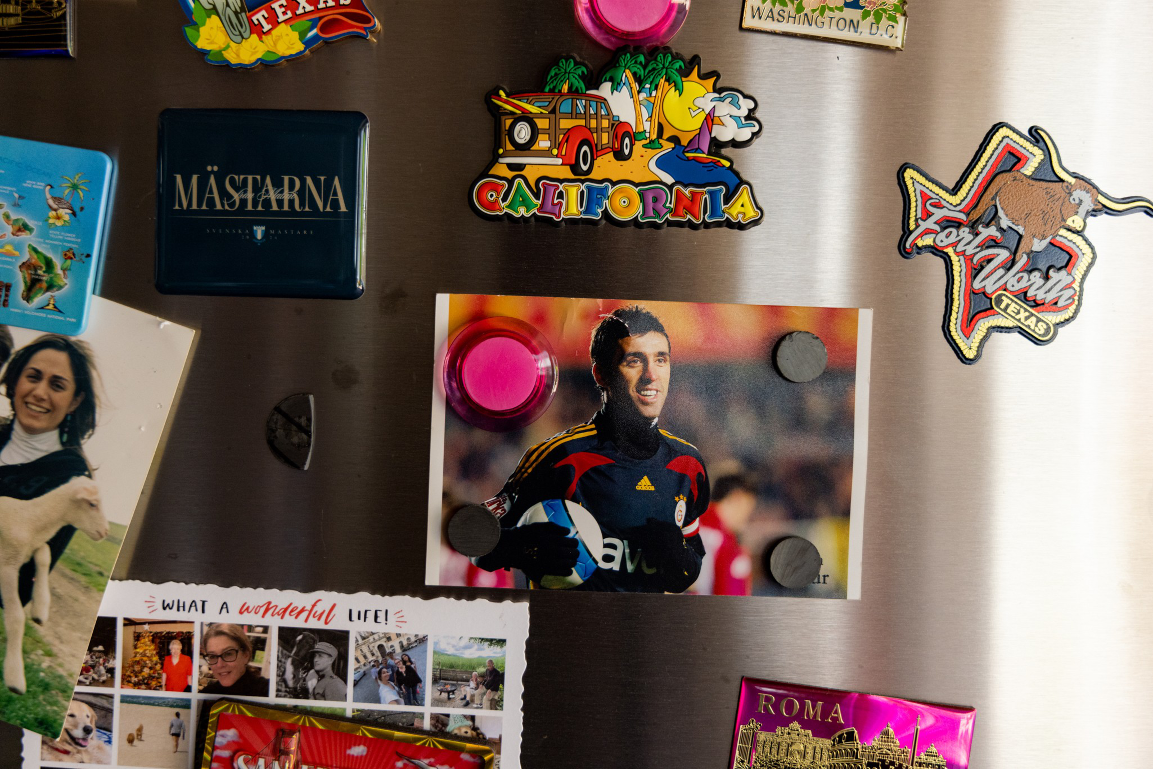 Colorful fridge magnets display Texas, California, Washington, D.C., and Roma; a photo of a man in a soccer jersey is held by round magnets.