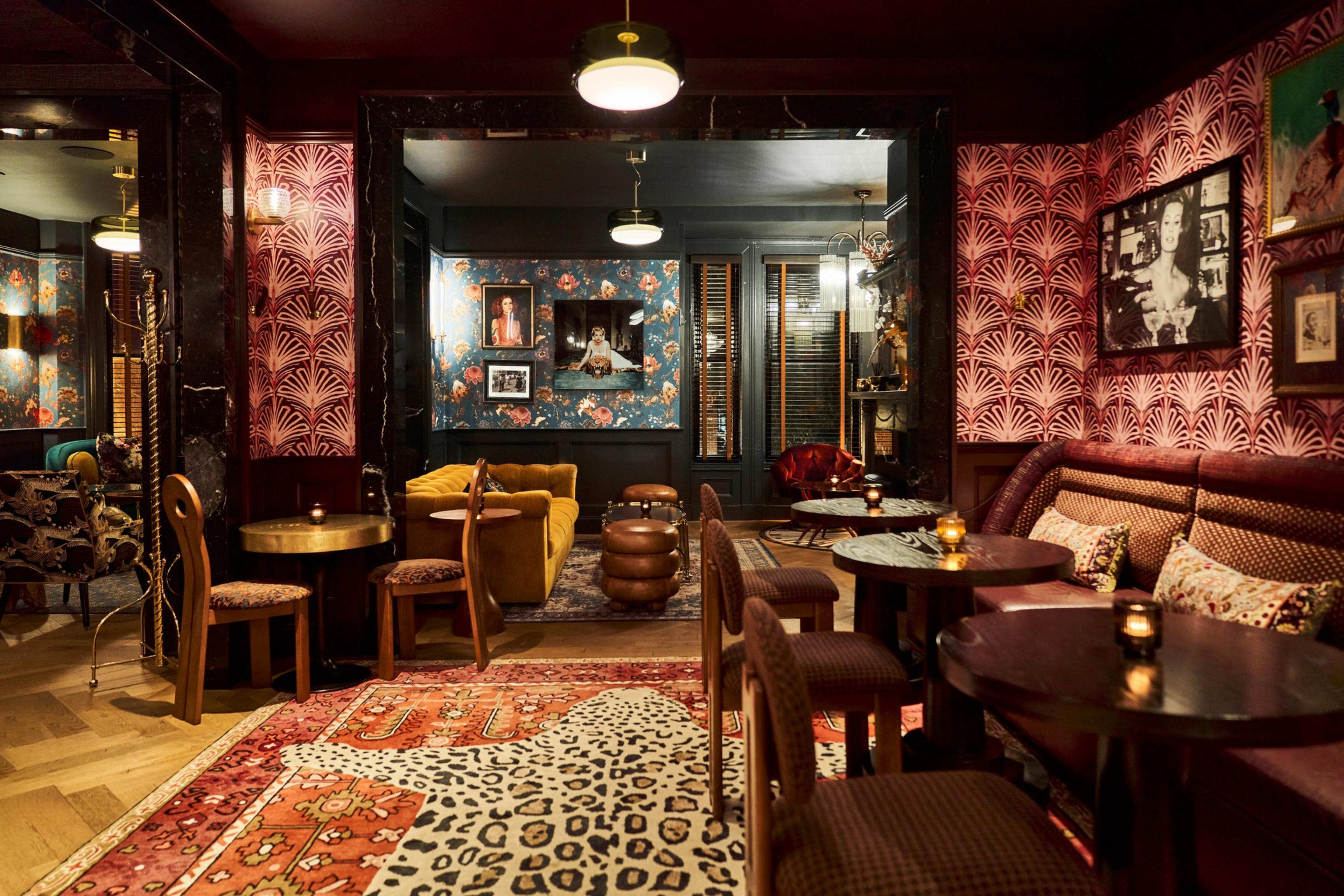 A room with patterned wallpaper, low tables, and comfortable chairs that sit on layered rugs.