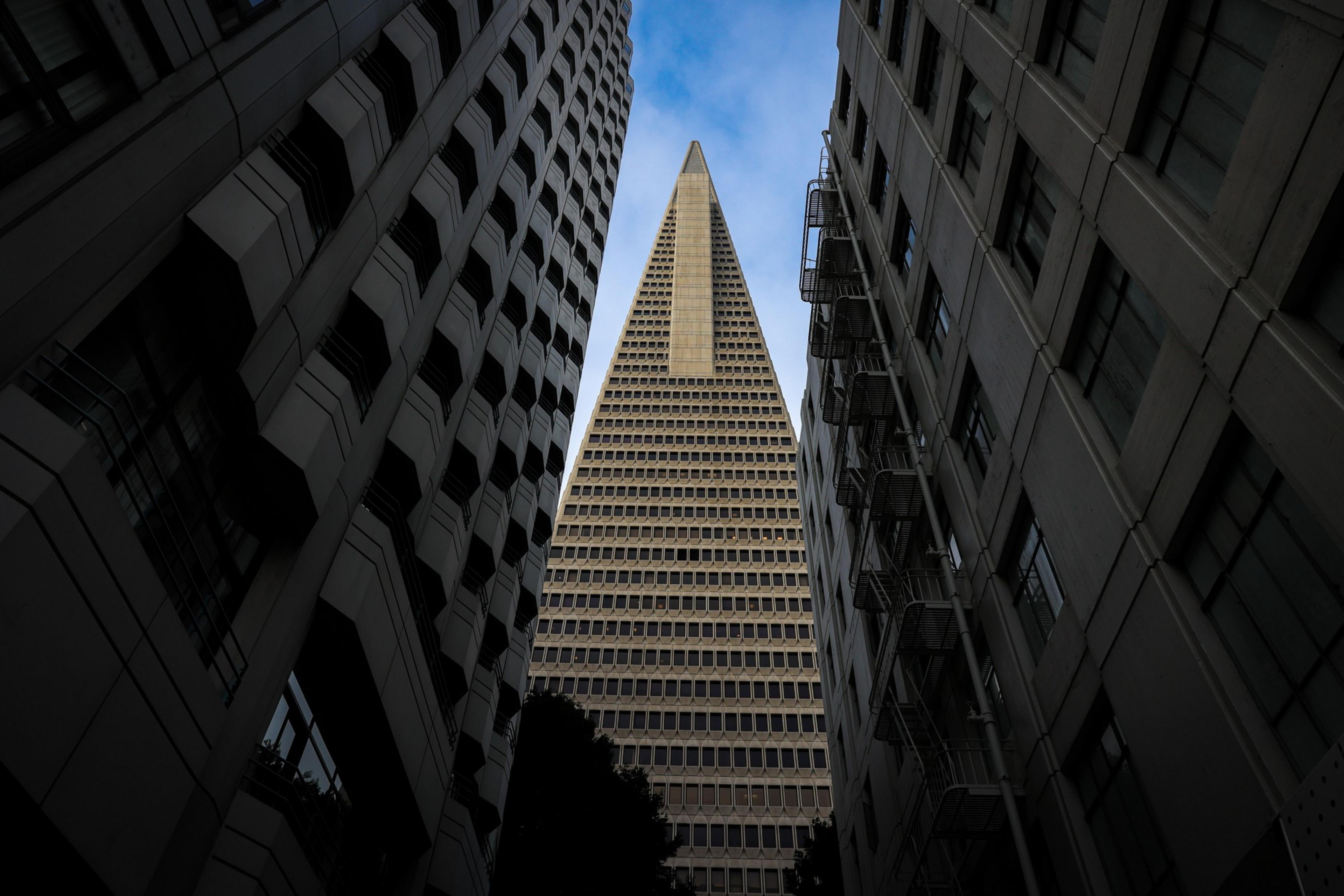 A towering skyscraper framed by two buildings under a blue sky, presenting a striking urban perspective.