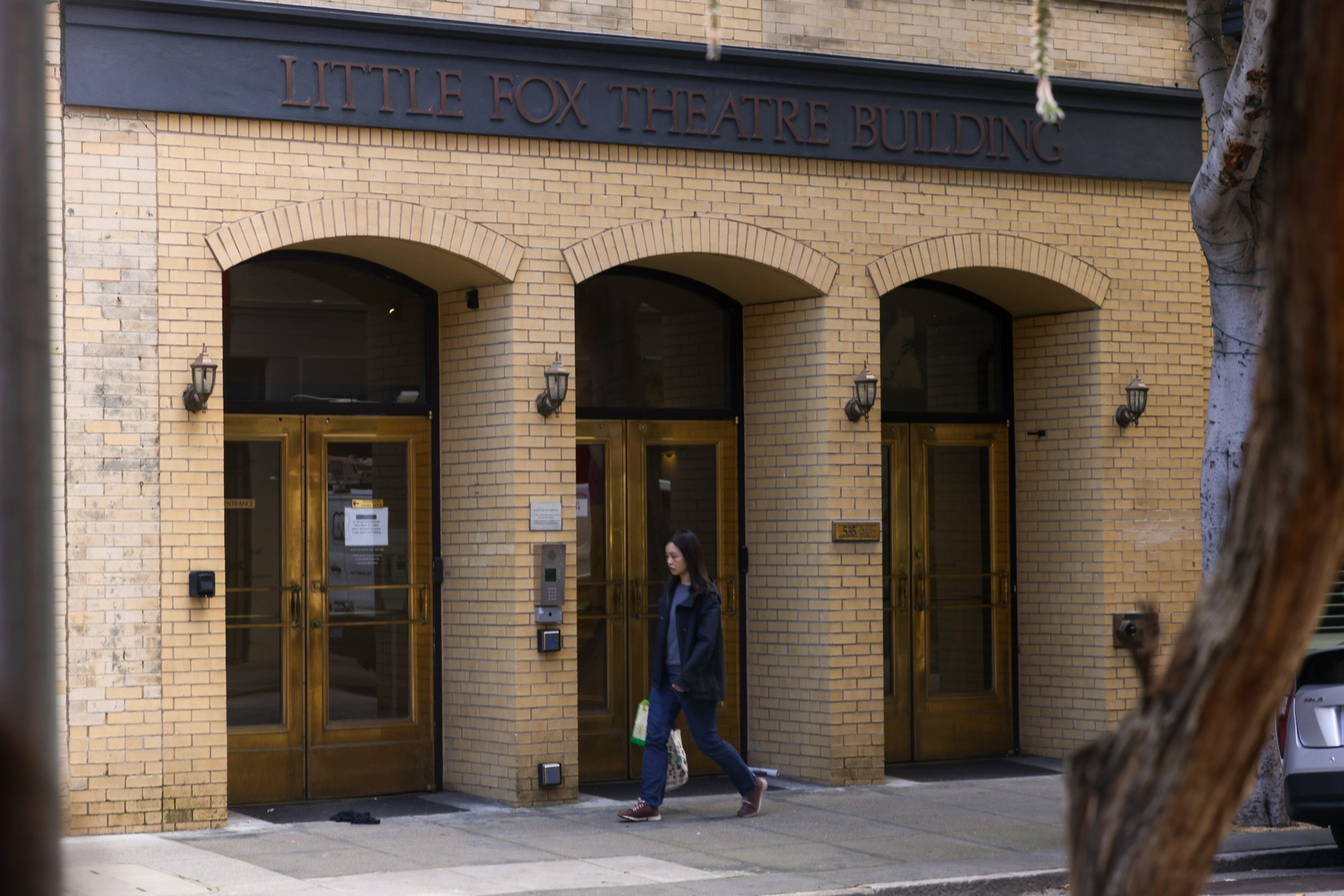 A person walks by the entrance of the &quot;Little Fox Theatre Building&quot; with arched doorways.