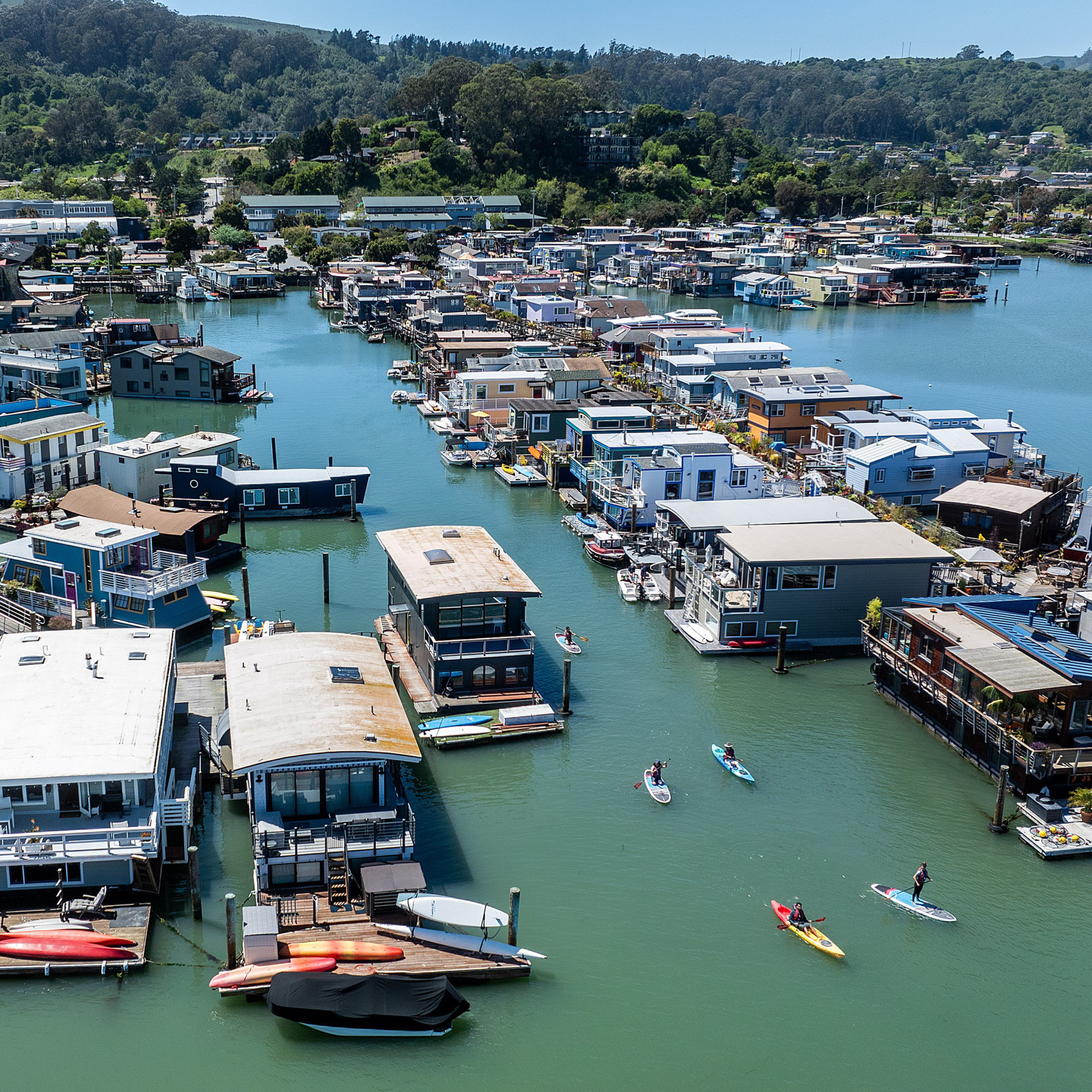 Aerial view of a colorful floating homes community with people kayaking on the water.