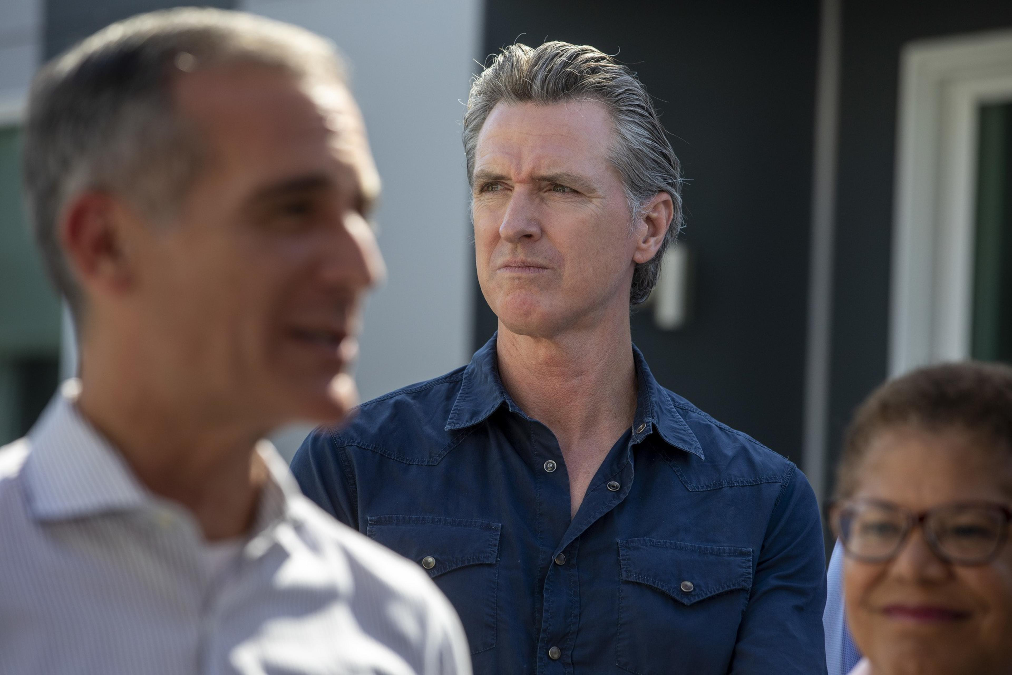 A man in a blue shirt looks off in the distance, flanked by 2 people