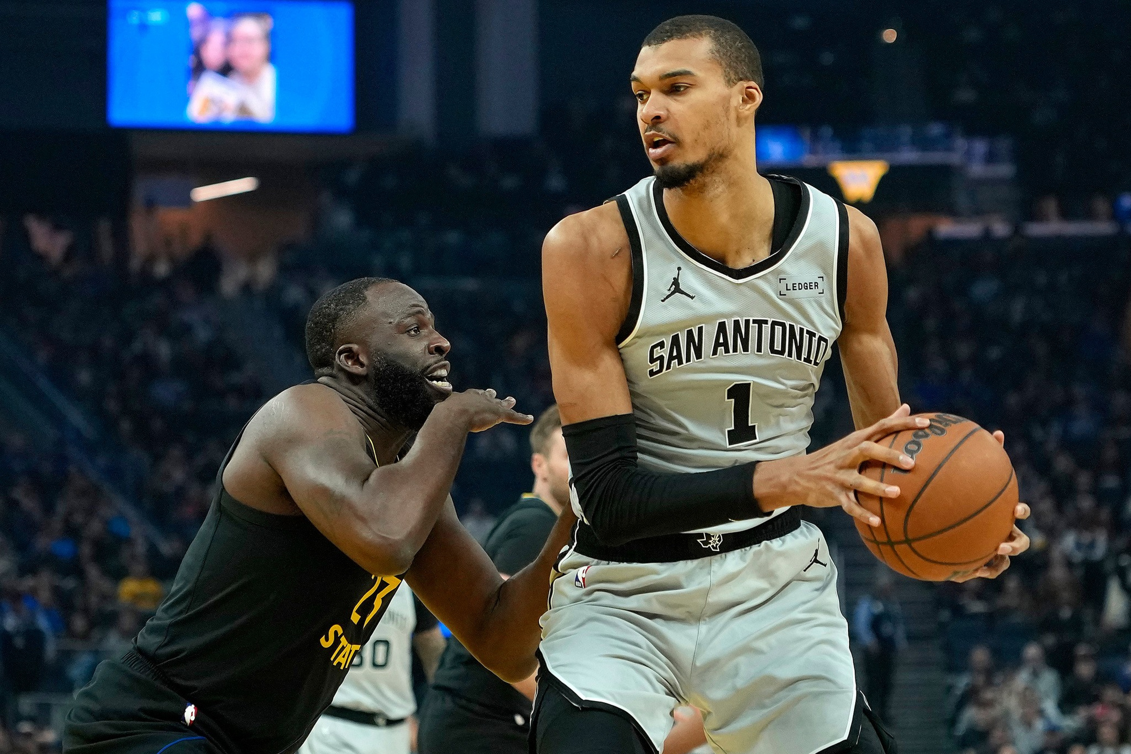 A San Antonio basketball player holds the ball while being closely guarded by a Golden State player during a game.