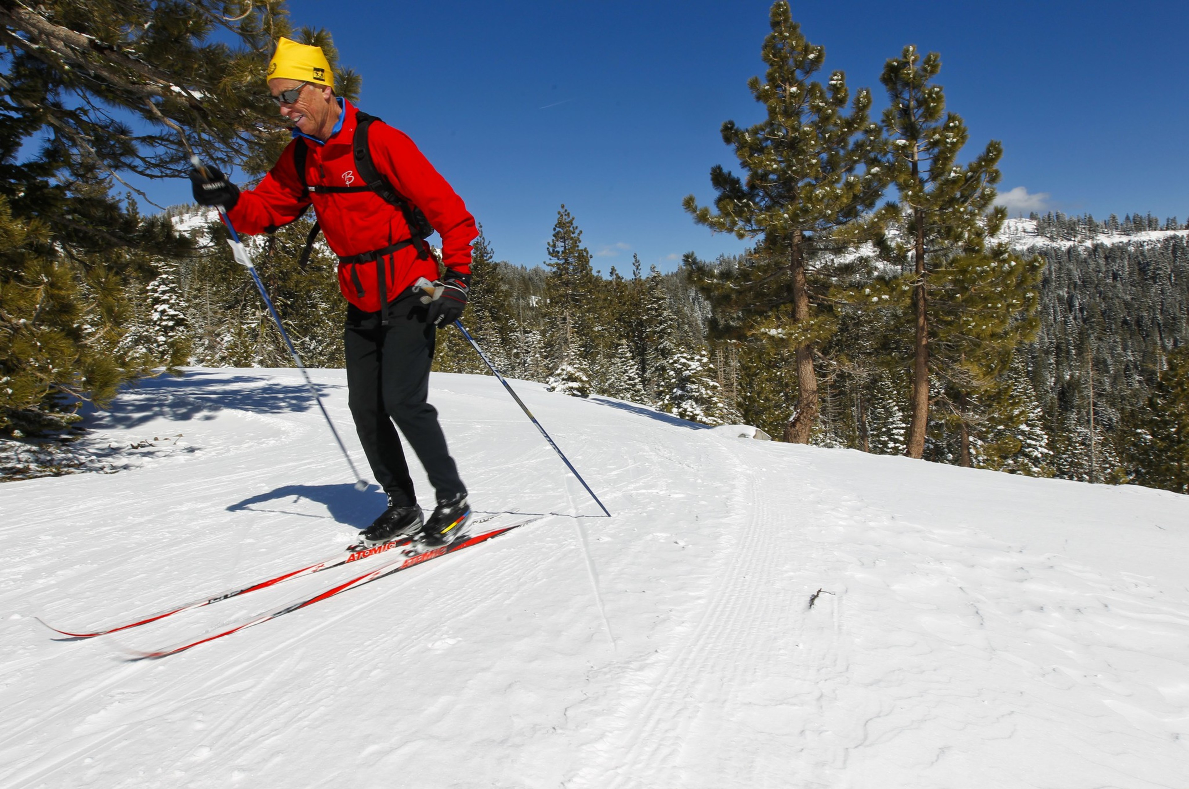 A man in a red jacket cross-country skis with a smile on his face