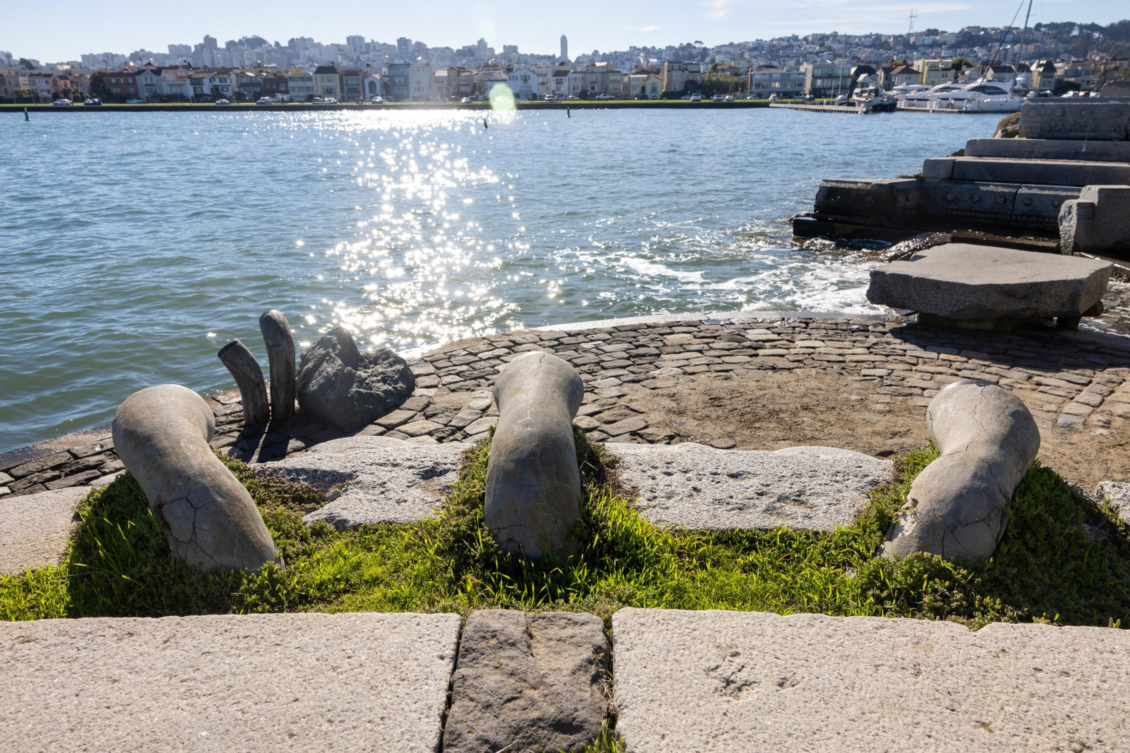 Light glints off the water by a jetty that has a concrete and stone structure on it. 