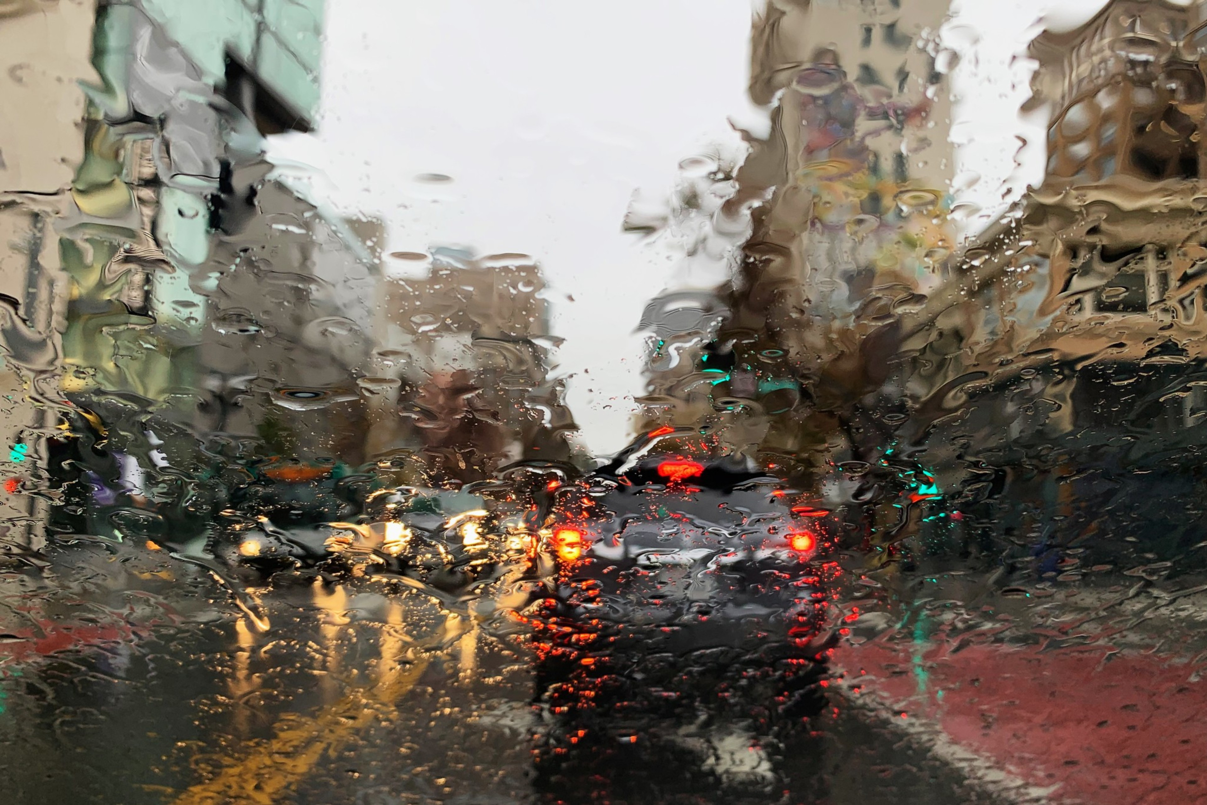 Raindrops cover the windshield of a car at a stoplight.